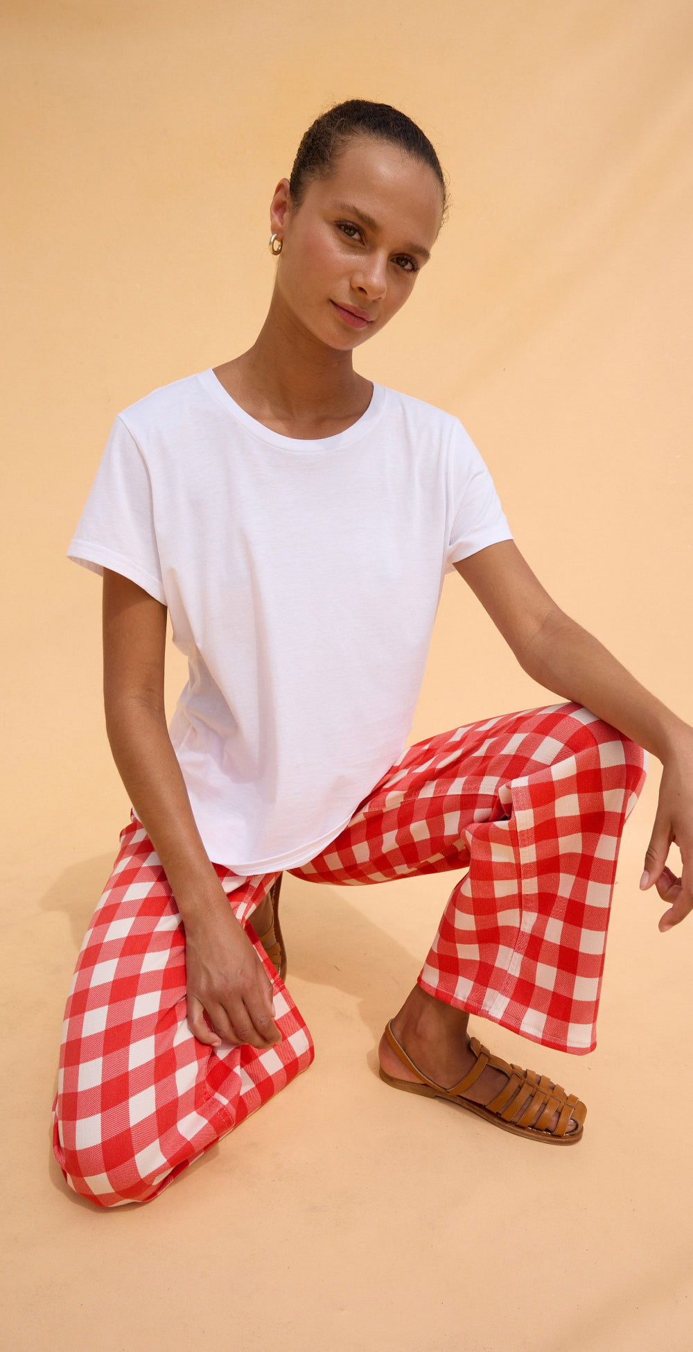 Woman wearing a white t-shirt and red checkered pants on a beige background