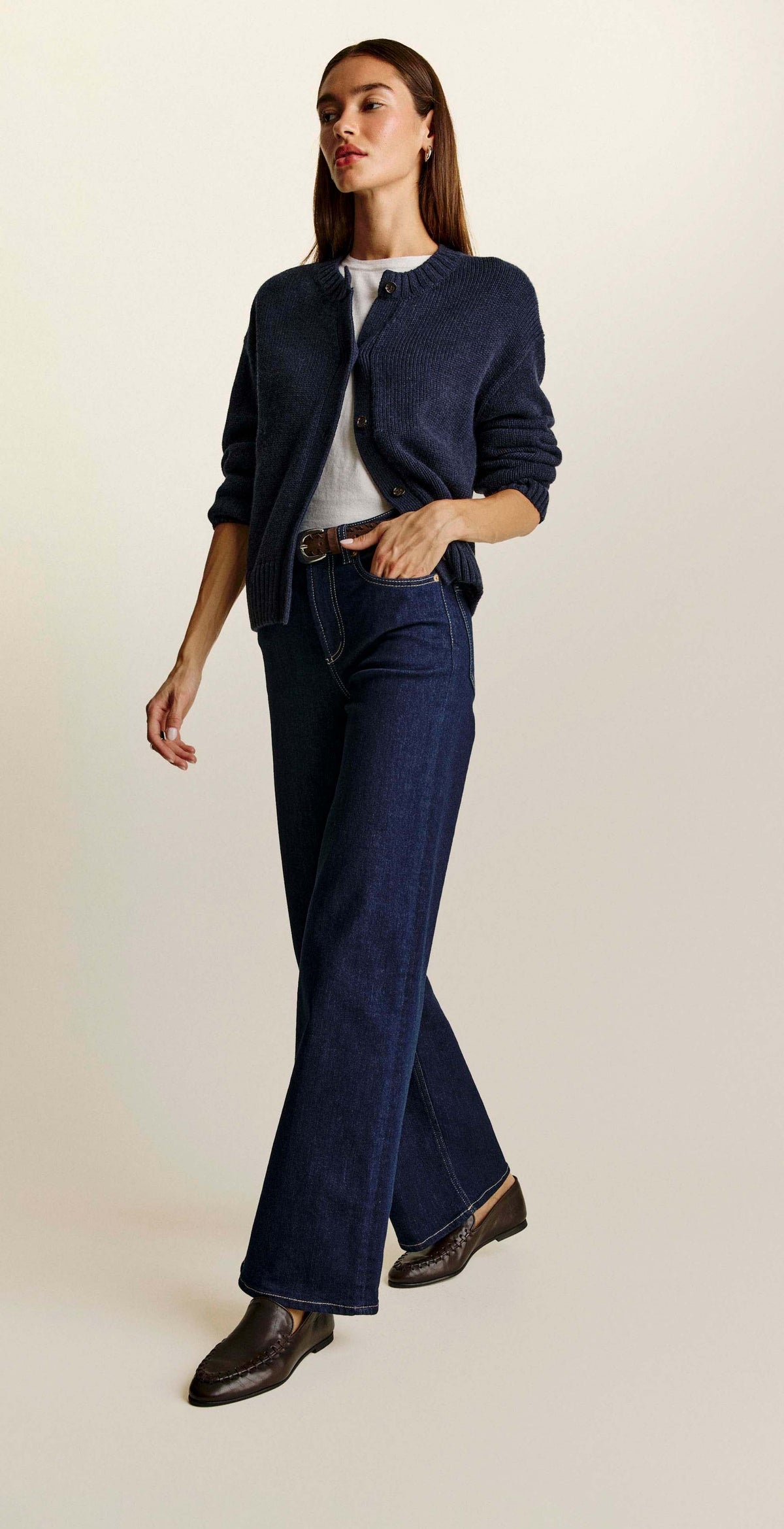 A three-panel collage showing a woman modeling a dark navy cardigan, dark navy wide-leg jeans, a white top, and a brown belt against a plain light beige studio background.