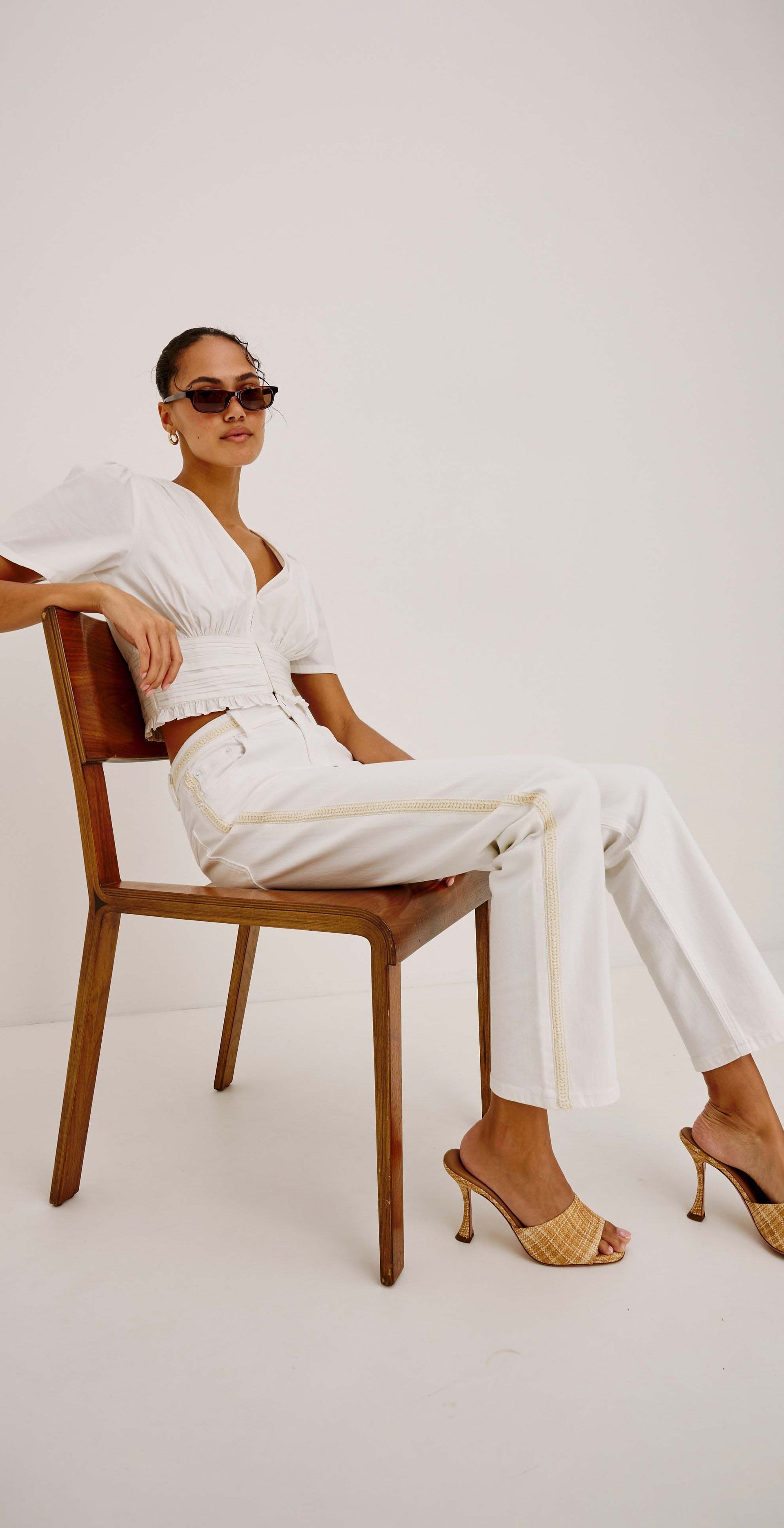 Woman in a white outfit sitting on a wooden chair against a white background