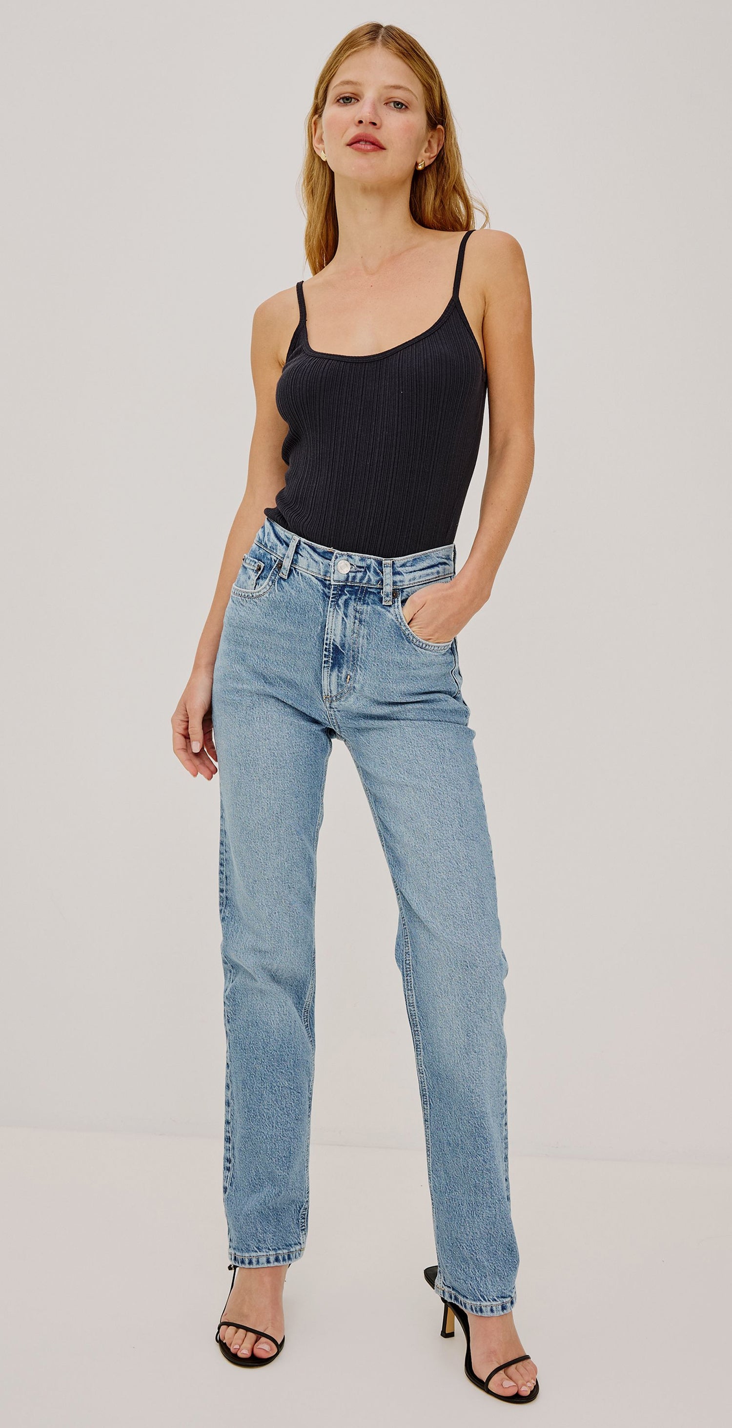 Woman wearing a black tank top and light blue jeans on a plain background