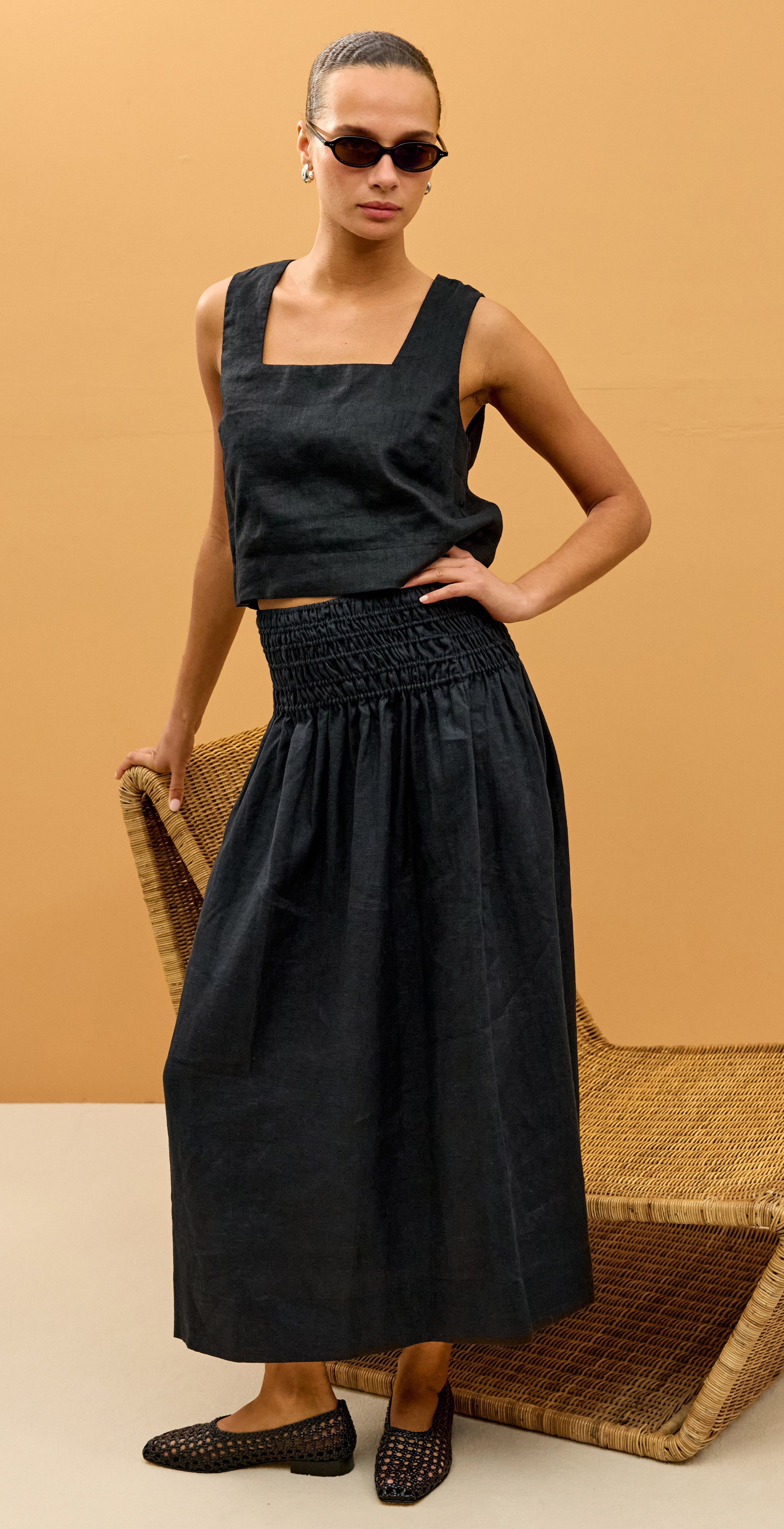 Woman wearing a black sleeveless top and skirt set against a beige background