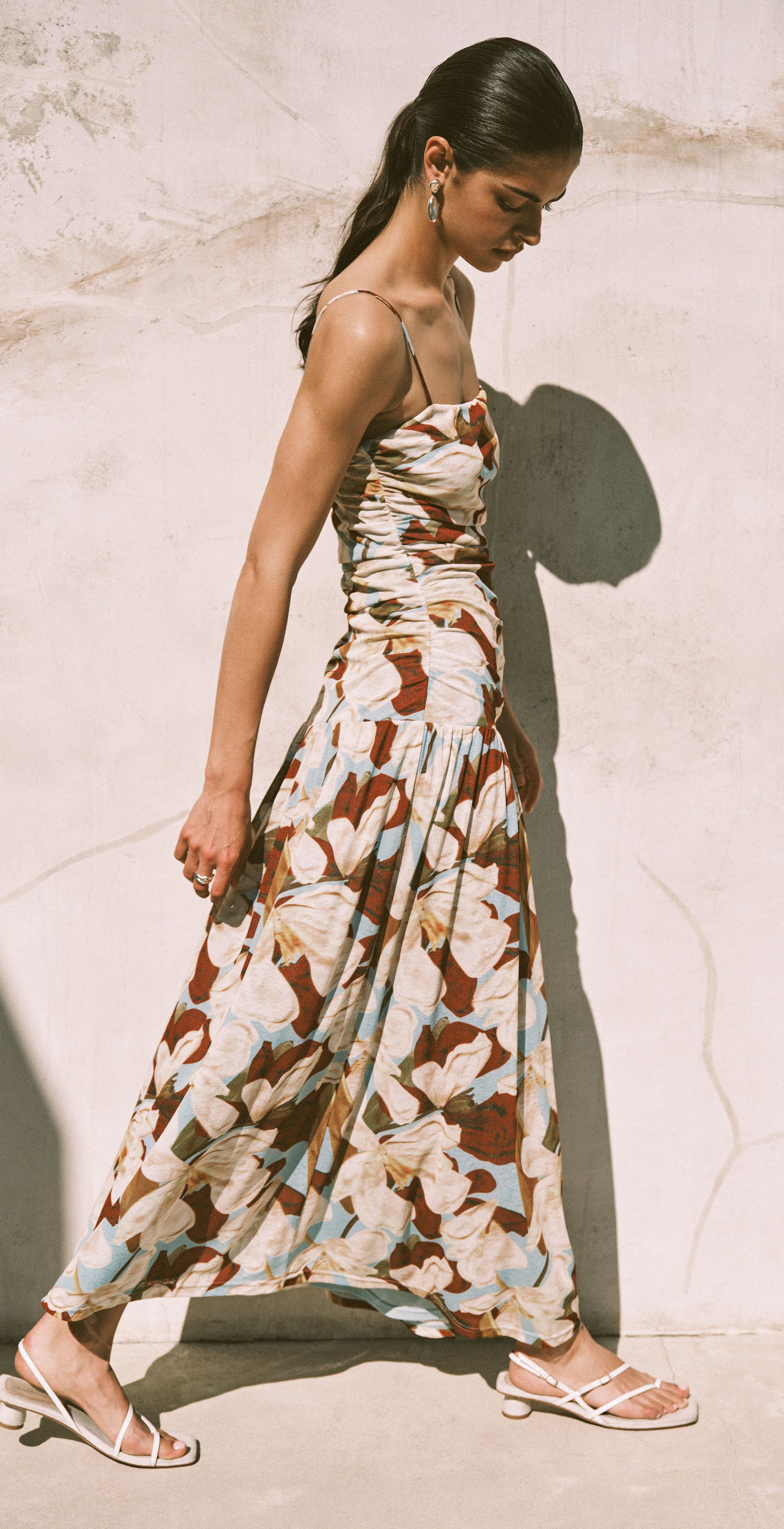 Woman in a patterned dress sitting against a textured wall.