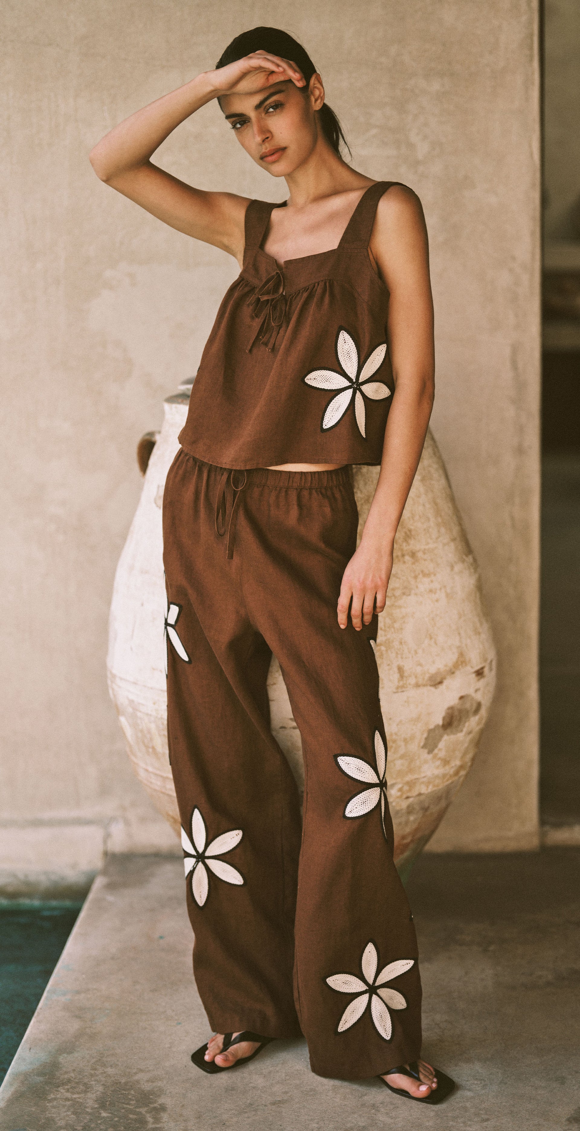 Woman wearing a brown outfit with white floral patterns in an outdoor setting.