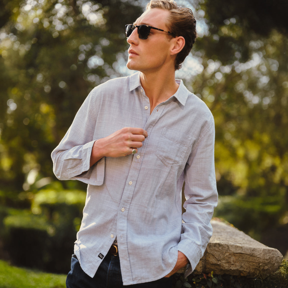 Man in a light blue button down shirt while looking away in a garden setting