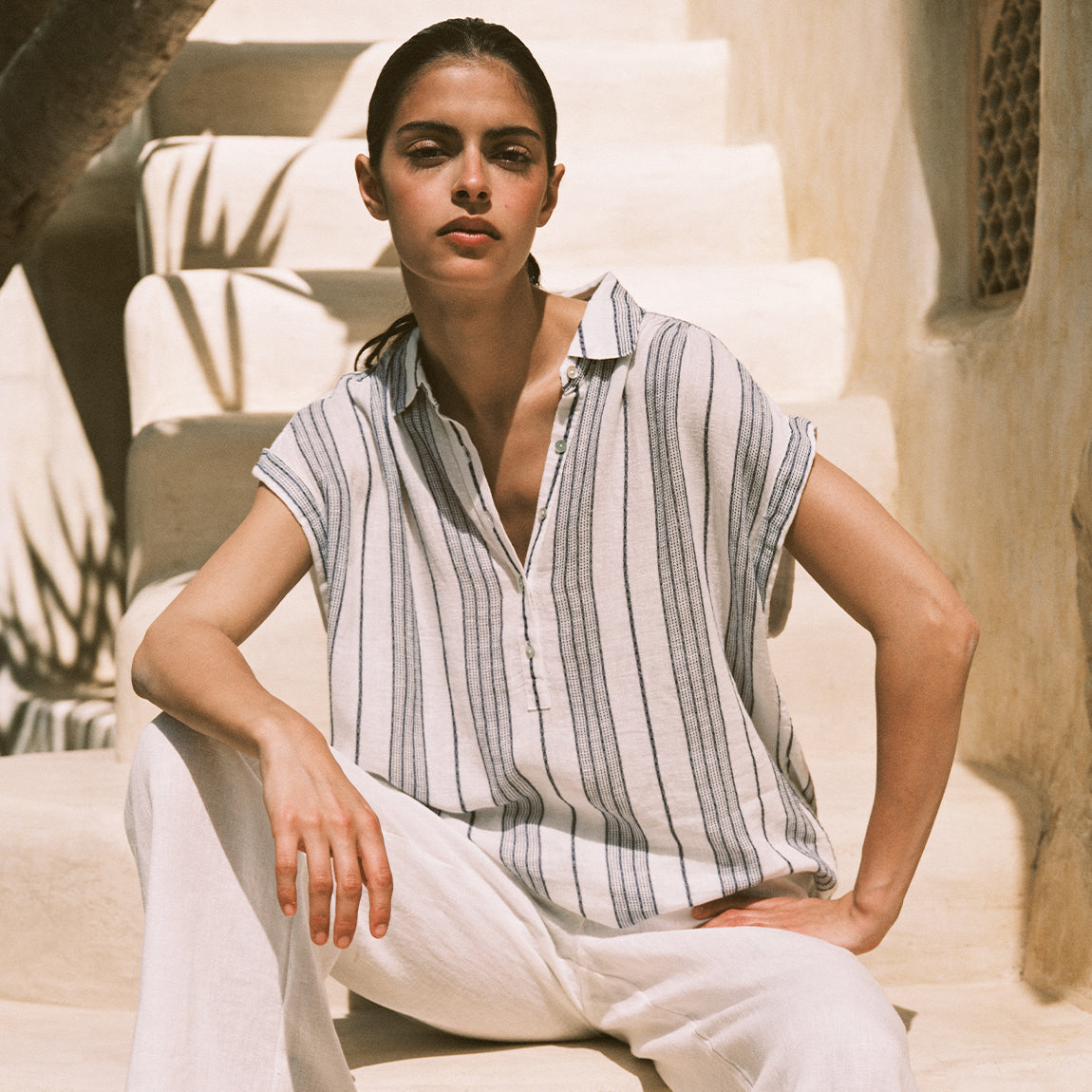 Woman wearing a striped shirt and white pants sitting on a staircase.