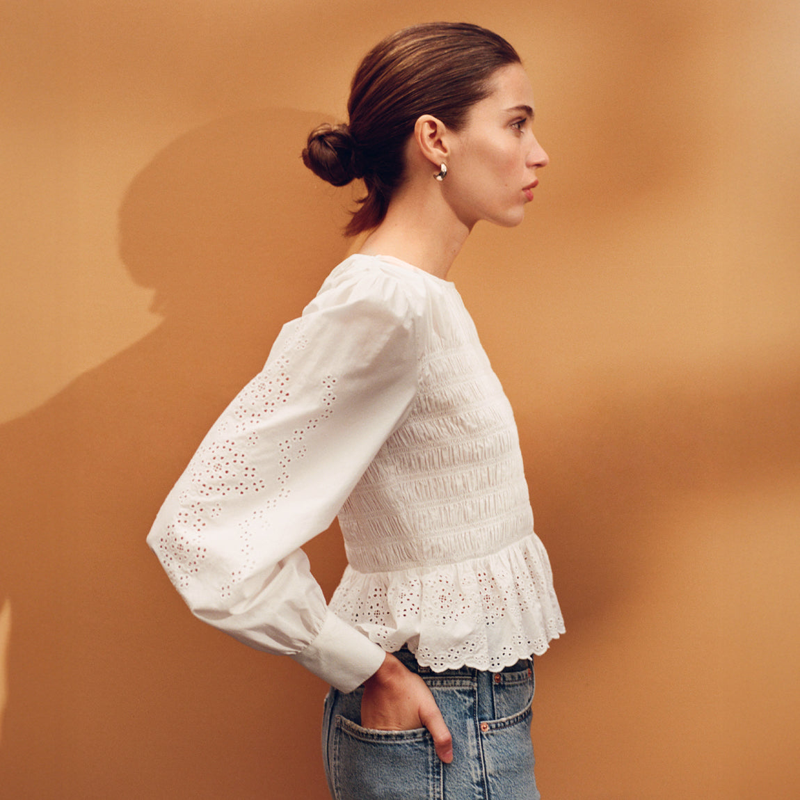 Woman wearing a white blouse with long sleeves and ruffled hem against a brown background