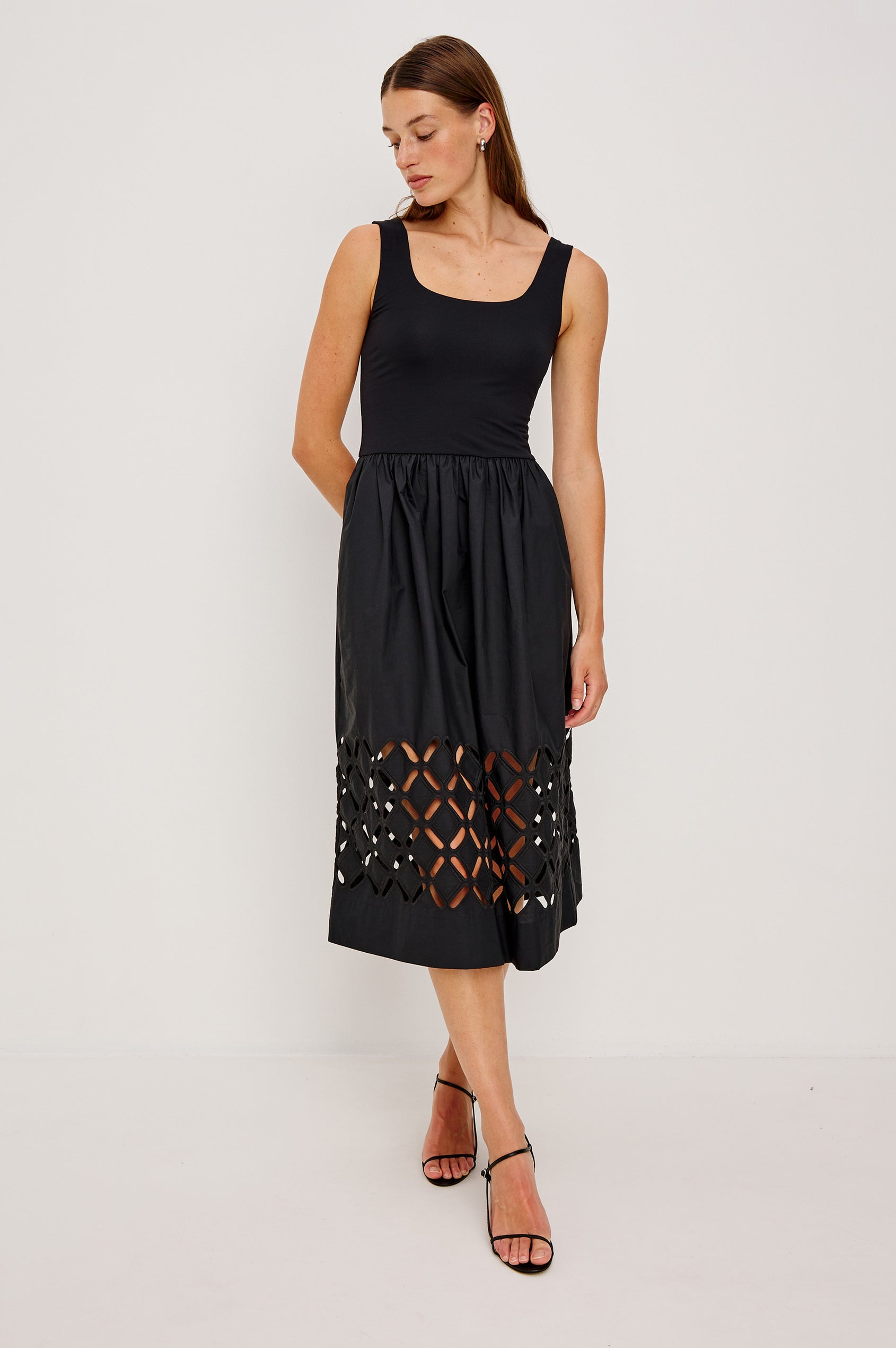 Nadya is a midi dress with a soft scoop neck bodice and a lightweight skirt in Black Colorway. The skirt features engineered cutouts from mid-thigh to hem and includes discreet on-seam pockets. Full Body front view featured on model.