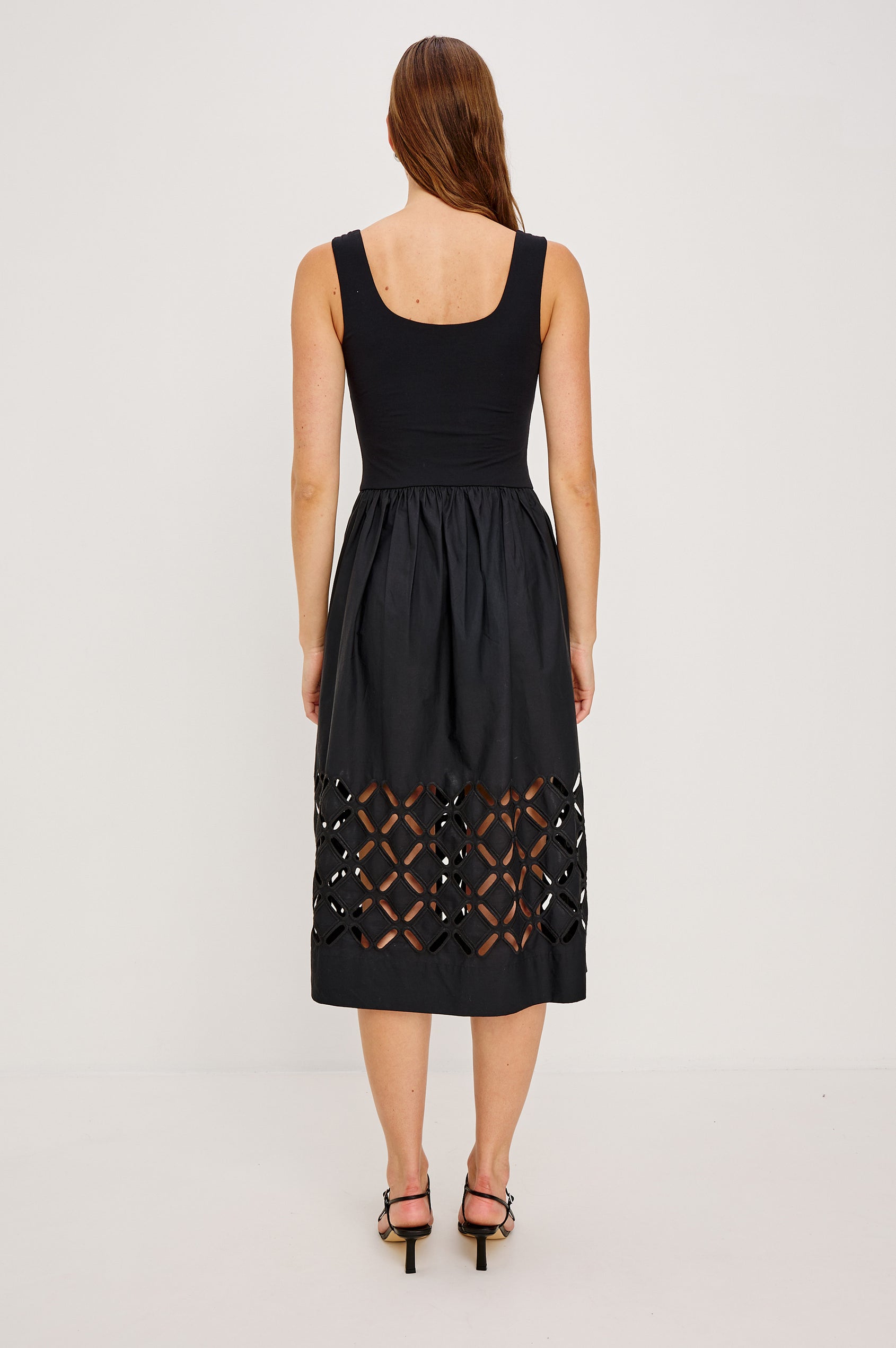 Nadya is a midi dress with a soft scoop neck bodice and a lightweight skirt in Black Colorway. The skirt features engineered cutouts from mid-thigh to hem and includes discreet on-seam pockets. Full Body back view featured on model.