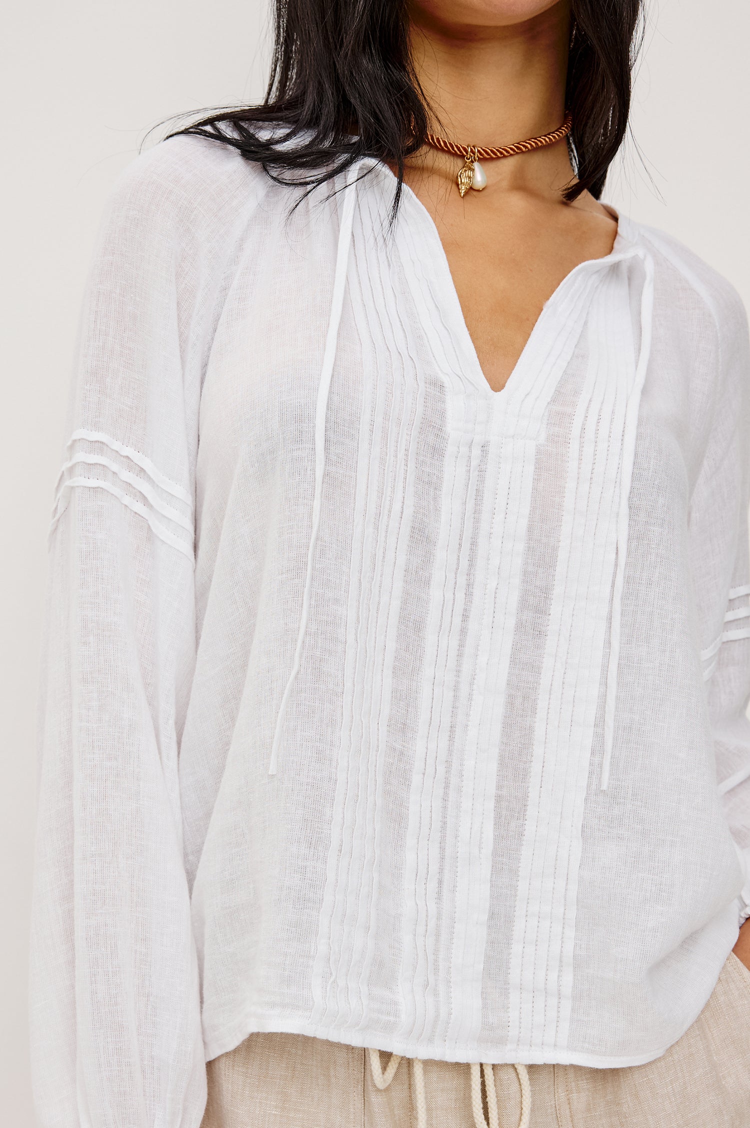Naples Top in Linen With Split V-Neckline With Self-Ties Long Billowing Sleeves With Fitted Cuffs Loose SIlhouettes and Intricate Seam Detailing in White Colorway - Upper Body Close Up Front View Featured on Model