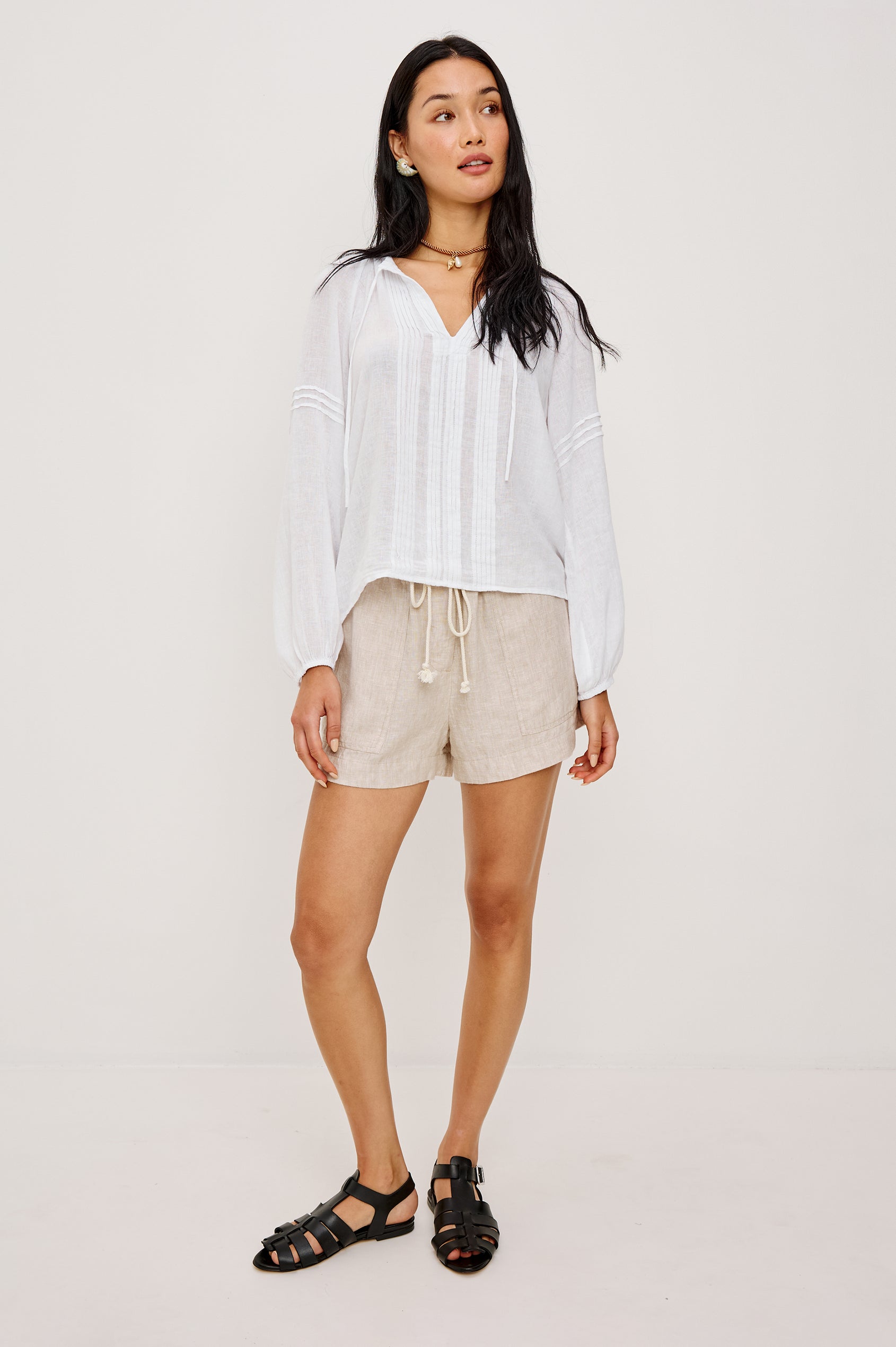 Naples Top in Linen With Split V-Neckline With Self-Ties Long Billowing Sleeves With Fitted Cuffs Loose SIlhouettes and Intricate Seam Detailing in White Colorway - Full Body Front View Featured on Model