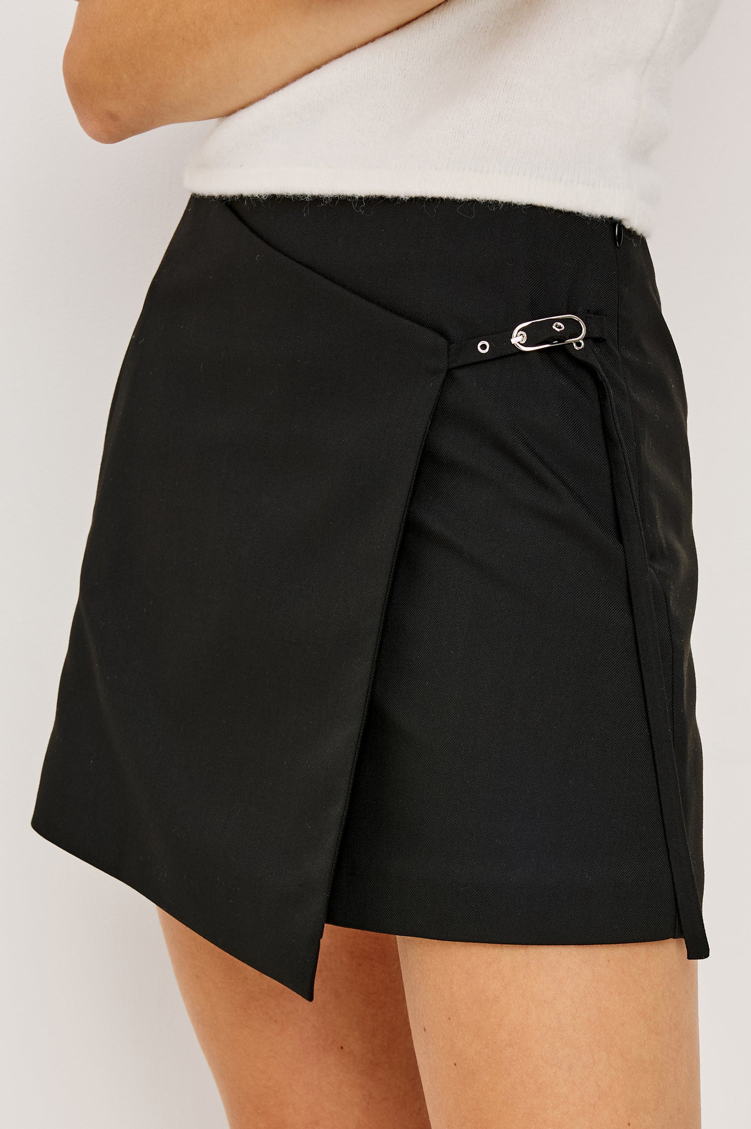 Nial is a mini faux-wrap skirt with an adjustable side buckle, side zip, decorative front pockets, and subtle back darting for shape in Black Twill Colorway. Close up of Details featured on model.