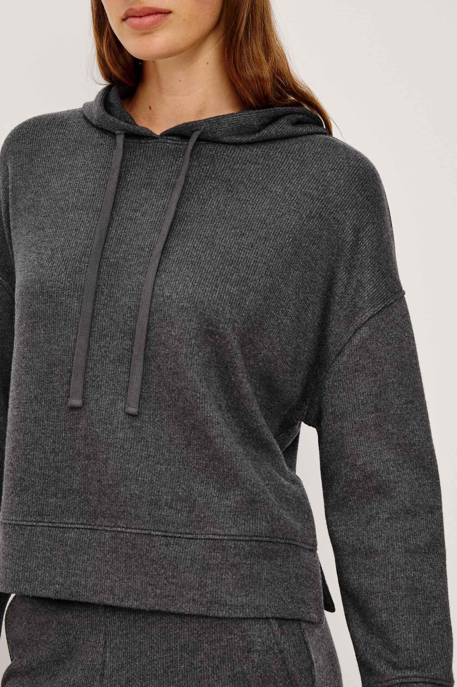 Nico is a hoodie in brushed rib lounge fabrication, with a relaxed fit and drop shoulders in charcoal colorway. Close up view featured on model.