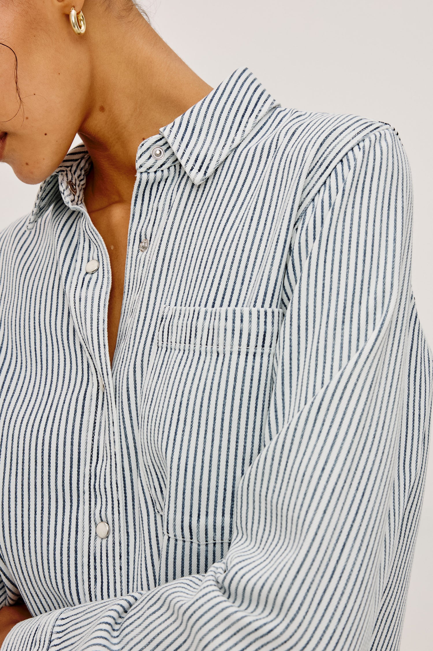 Noa Crop Denim Shirt With Boxy Fit, Front Snap Buttons, a Chest Patch Pocket, and Long Sleeves in Railroad Stripe Colorway - Upper Body Close Up Front View Featured on Model