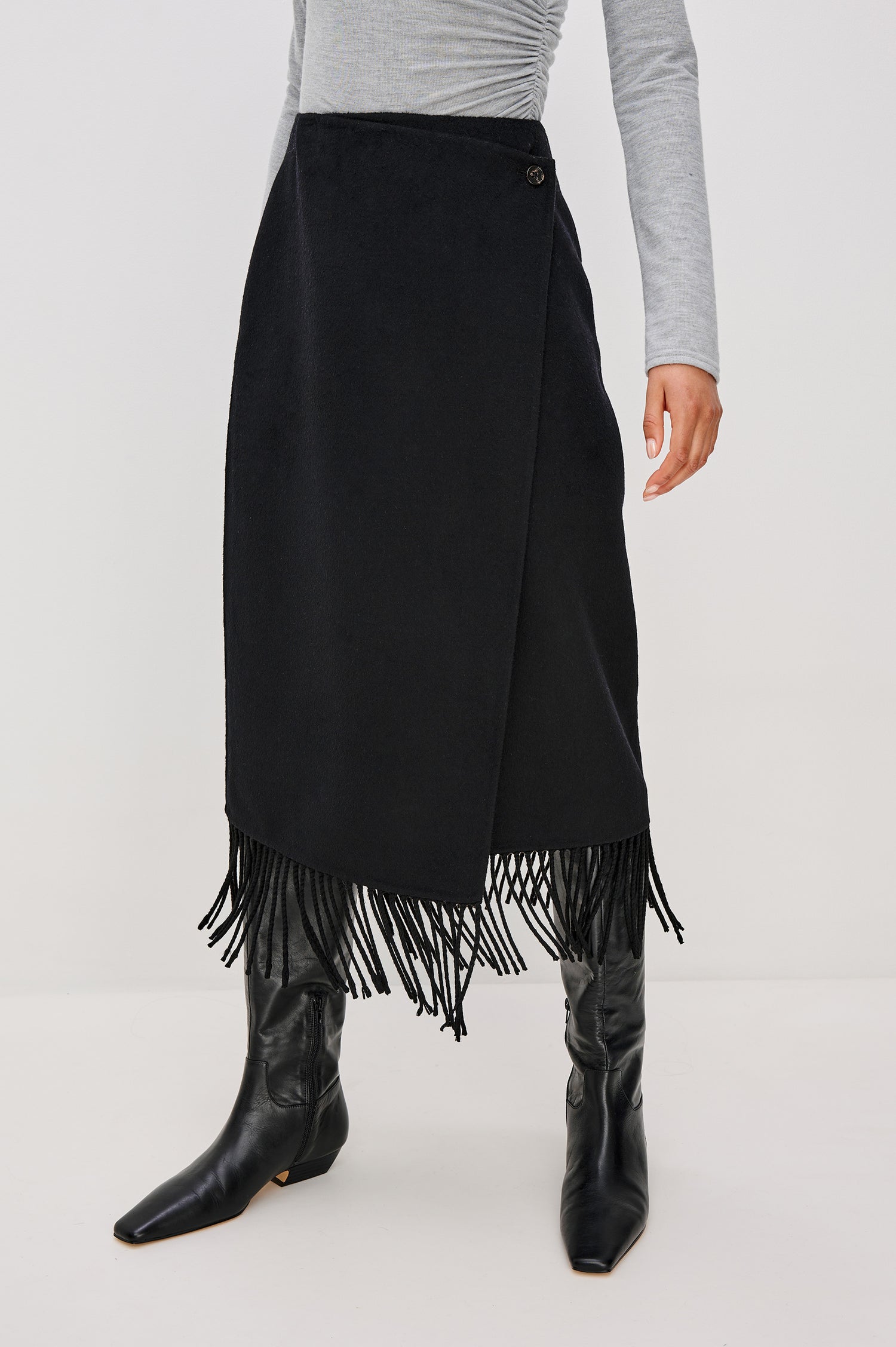 Odette Midi Skirt in Wool Blend With Wrap Design, Hidden Side Button Closure, and Fringe Hem in Black Colorway - Lower Body Front View Featured on Model