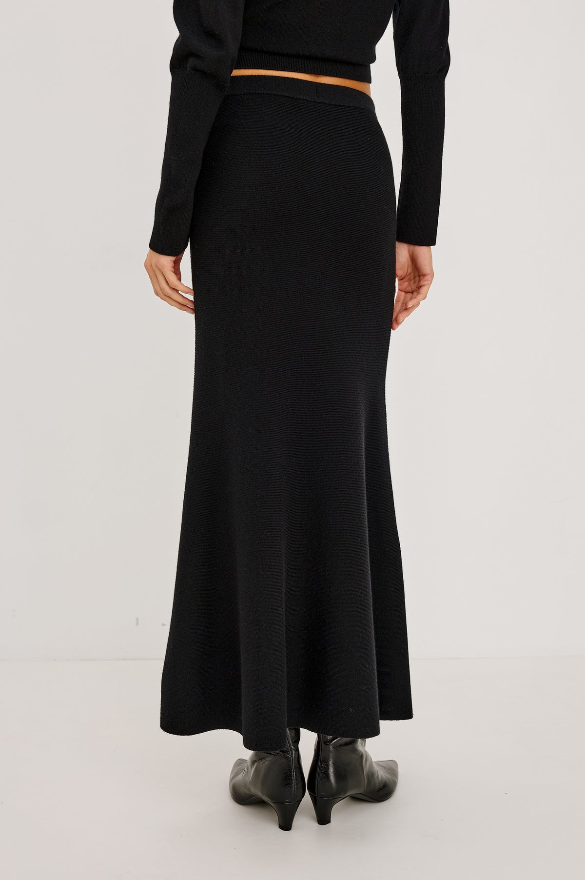 Odita Maxi Skirt in Soft Ribbed Wool Blend Knit With Elastic Waist, and A-Line Silhouette in Black Colorway - Back Crop View Featured on Model.