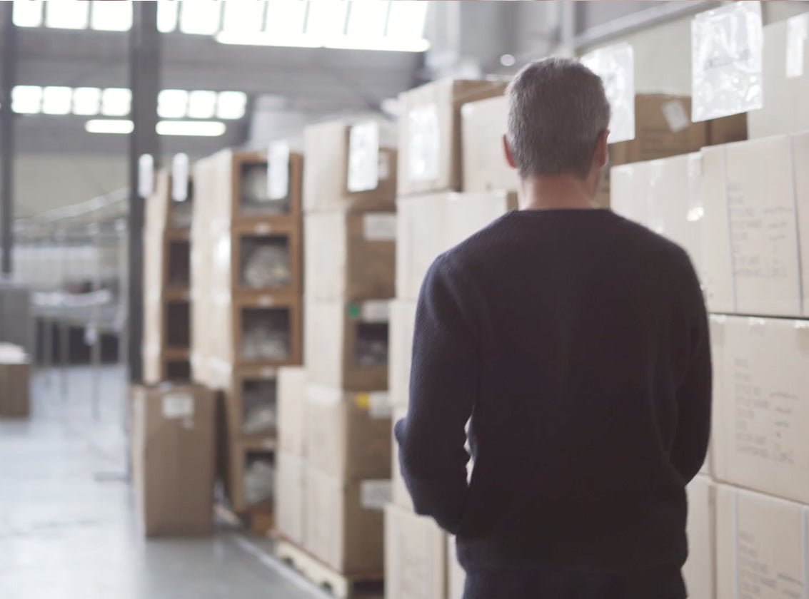 MAN WALKING THROUGH A WAREHOUSE SURROUNDED BY STACKED CARDBOARD BOXES