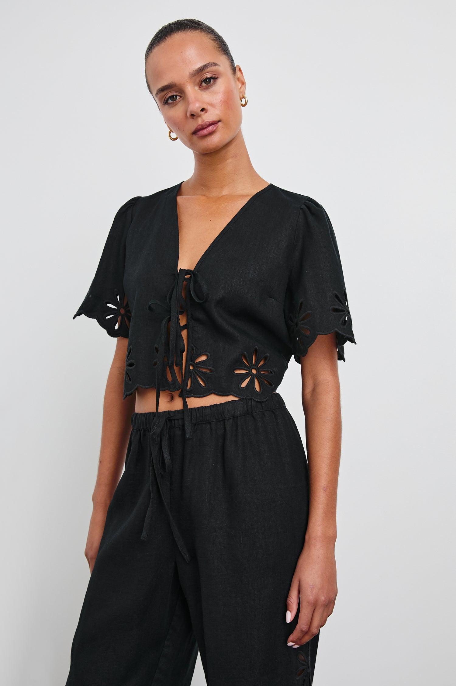 Pari Short-Sleeve Cropped Top with V Neck, Front Tie Closures, and Floral Eyelets in Black Eyelet Colorway - Front View Featured on Model 