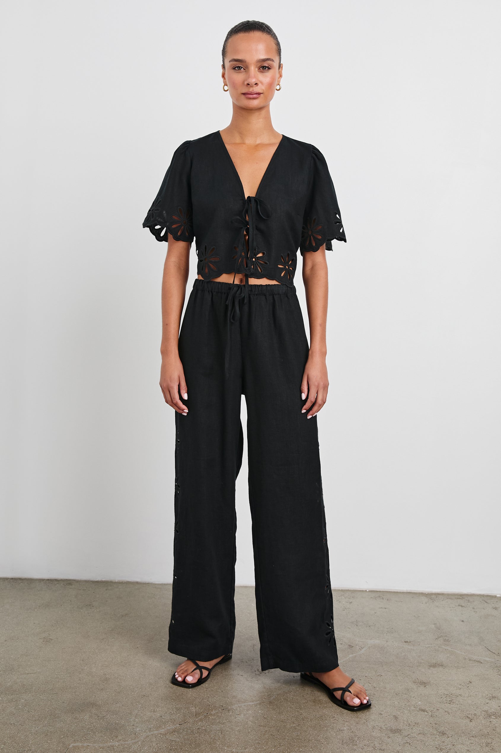 Pari Short-Sleeve Cropped Top with V Neck, Front Tie Closures, and Floral Eyelets in Black Eyelet Colorway - Front Full Body View Featured on Model 