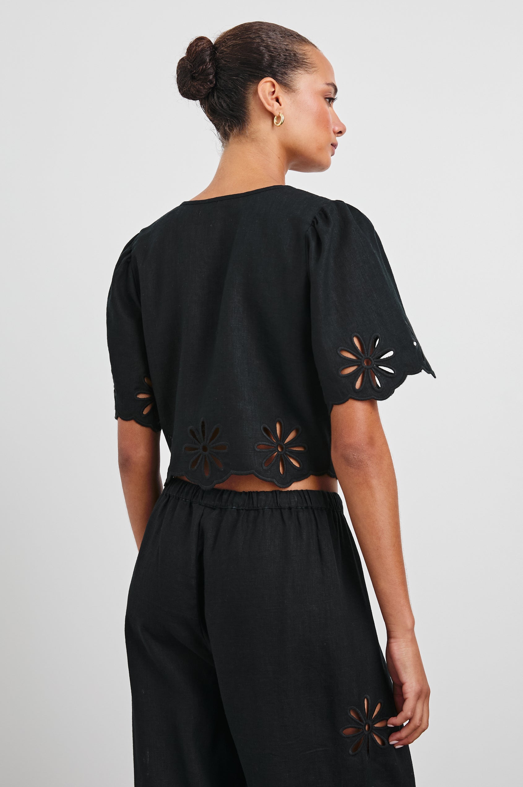 Pari Short-Sleeve Cropped Top with V Neck, Front Tie Closures, and Floral Eyelets in Black Eyelet Colorway - Back View Featured on Model 