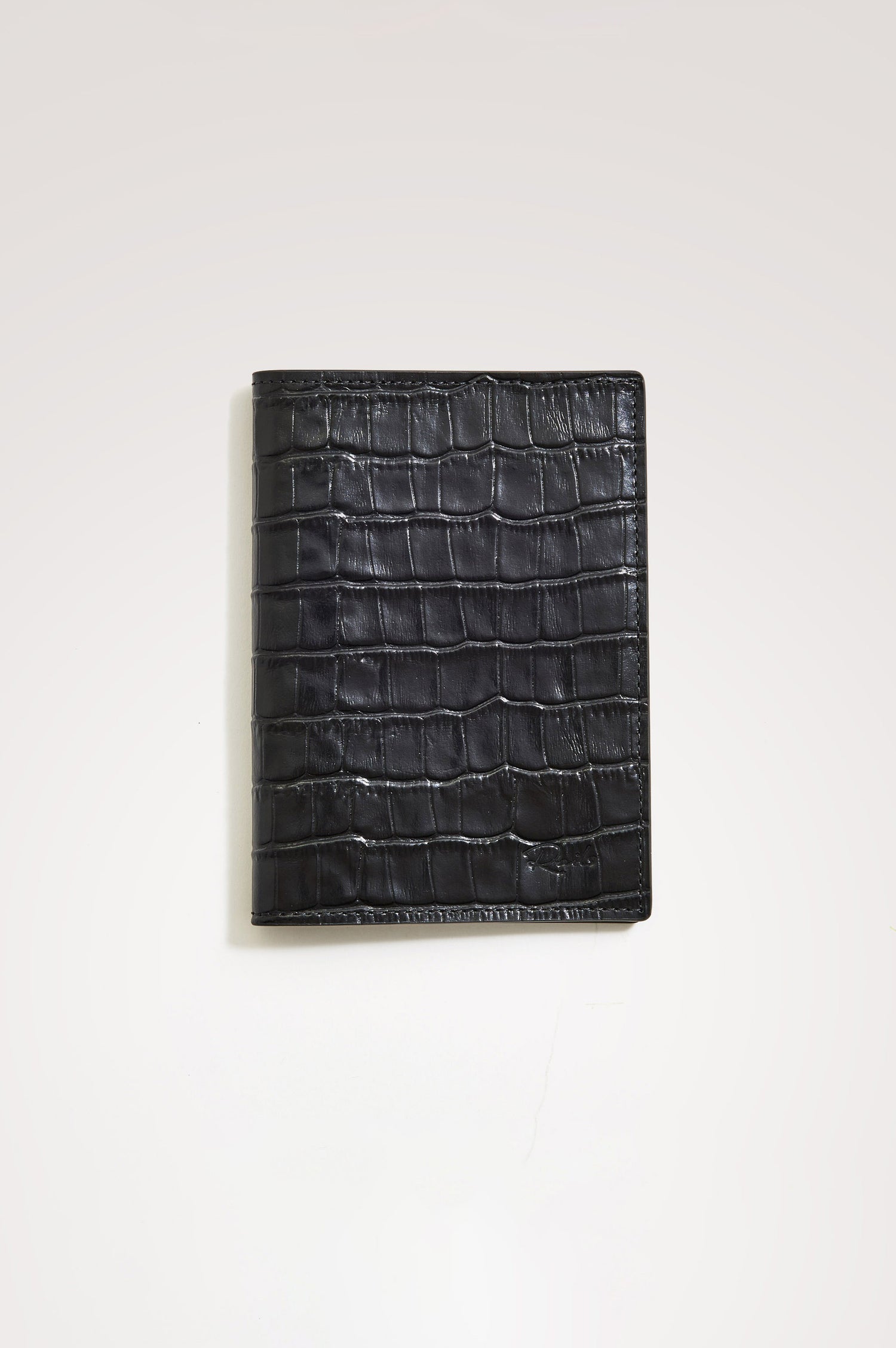 Passport Holder in Croc-Embossed Spanish Leather With Five Card Slots, Two Side Pockets, and Embossed Rails Logo in Black Croc Embossed Colorway - Front view flatlay featured.