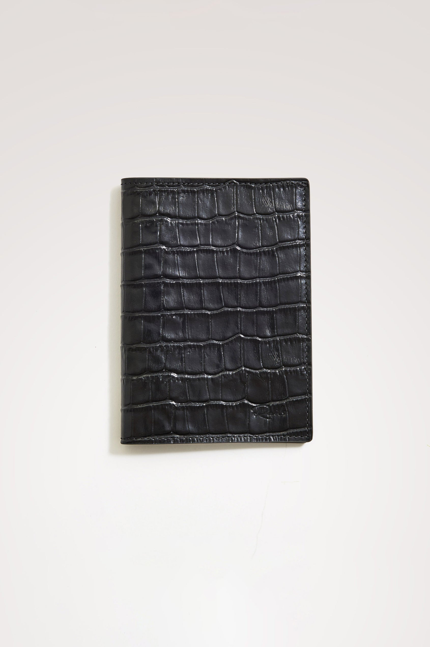 Passport Holder in Croc-Embossed Spanish Leather With Five Card Slots, Two Side Pockets, and Embossed Rails Logo in Black Croc Embossed Colorway - Front view flatlay featured.