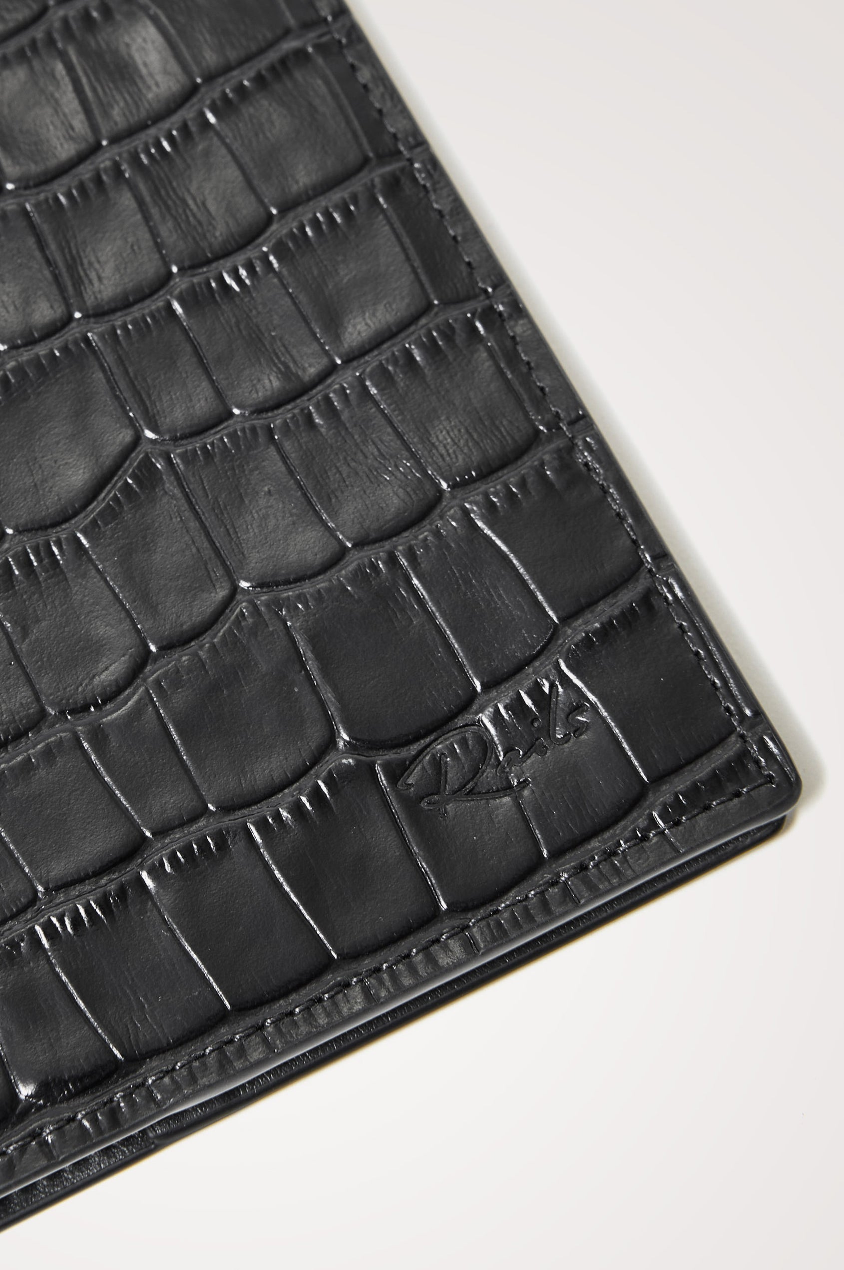 Passport Holder in Croc-Embossed Spanish Leather With Five Card Slots, Two Side Pockets, and Embossed Rails Logo in Black Croc Embossed Colorway - Front close-up flatlay view featured.