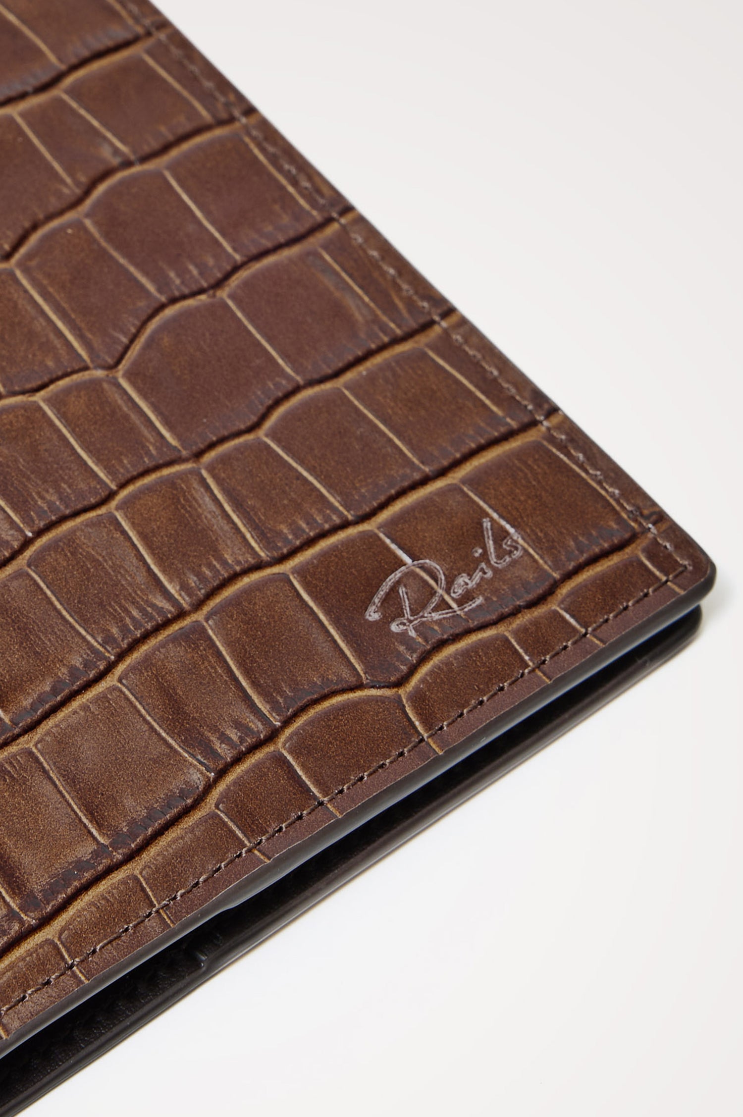 Passport Holder in Croc-Embossed Spanish Leather With Five Card Slots, Two Side Pockets, and Embossed Rails Logo in Dark Brown Croc Embossed Colorway - Front close-up flatlay view featured.