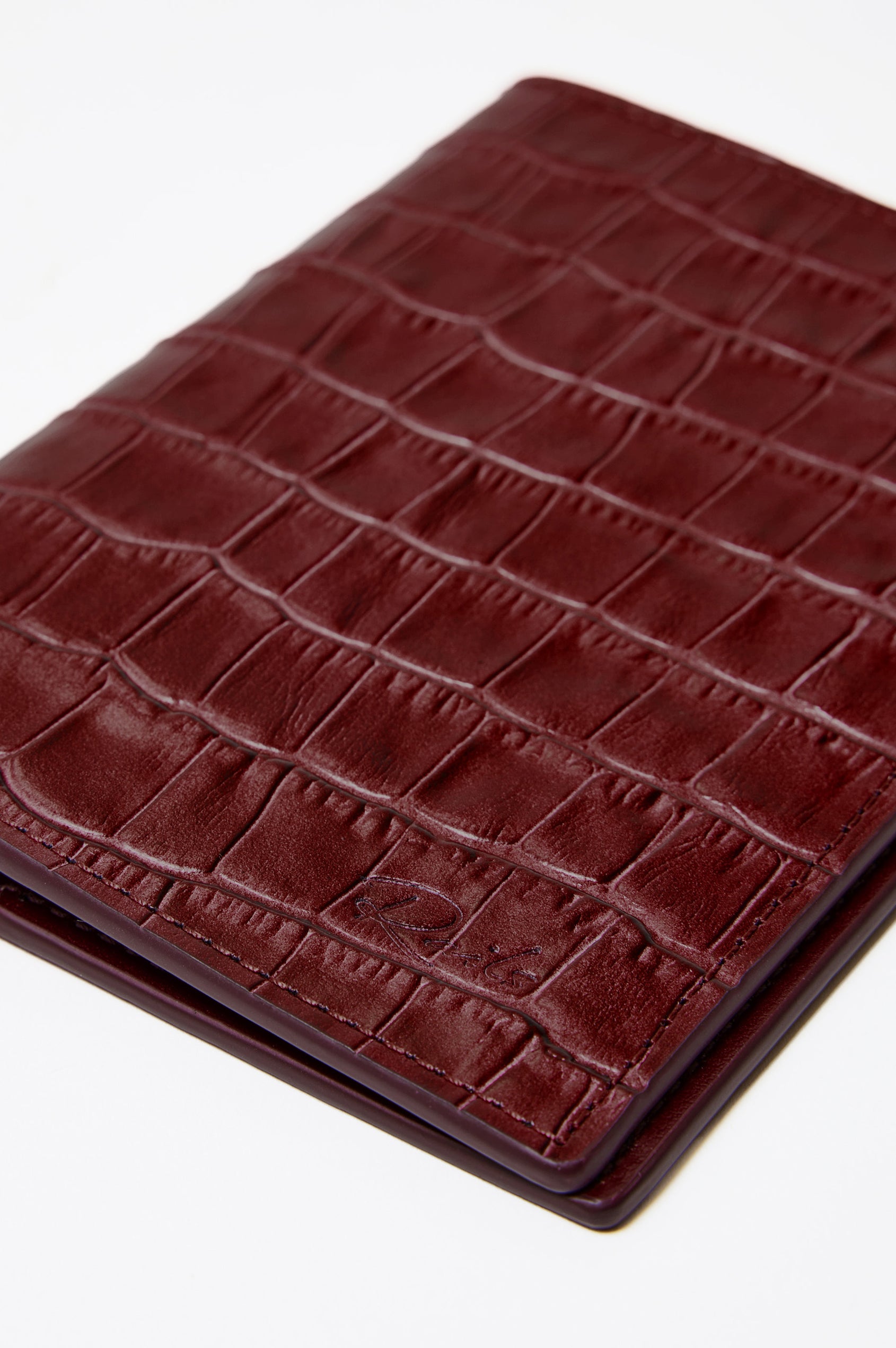 Passport Holder in Croc-Embossed Spanish Leather With Five Card Slots, Two Side Pockets, and Embossed Rails Logo in Burgundy Croc Embossed Colorway - Front close-up flatlay view featured.