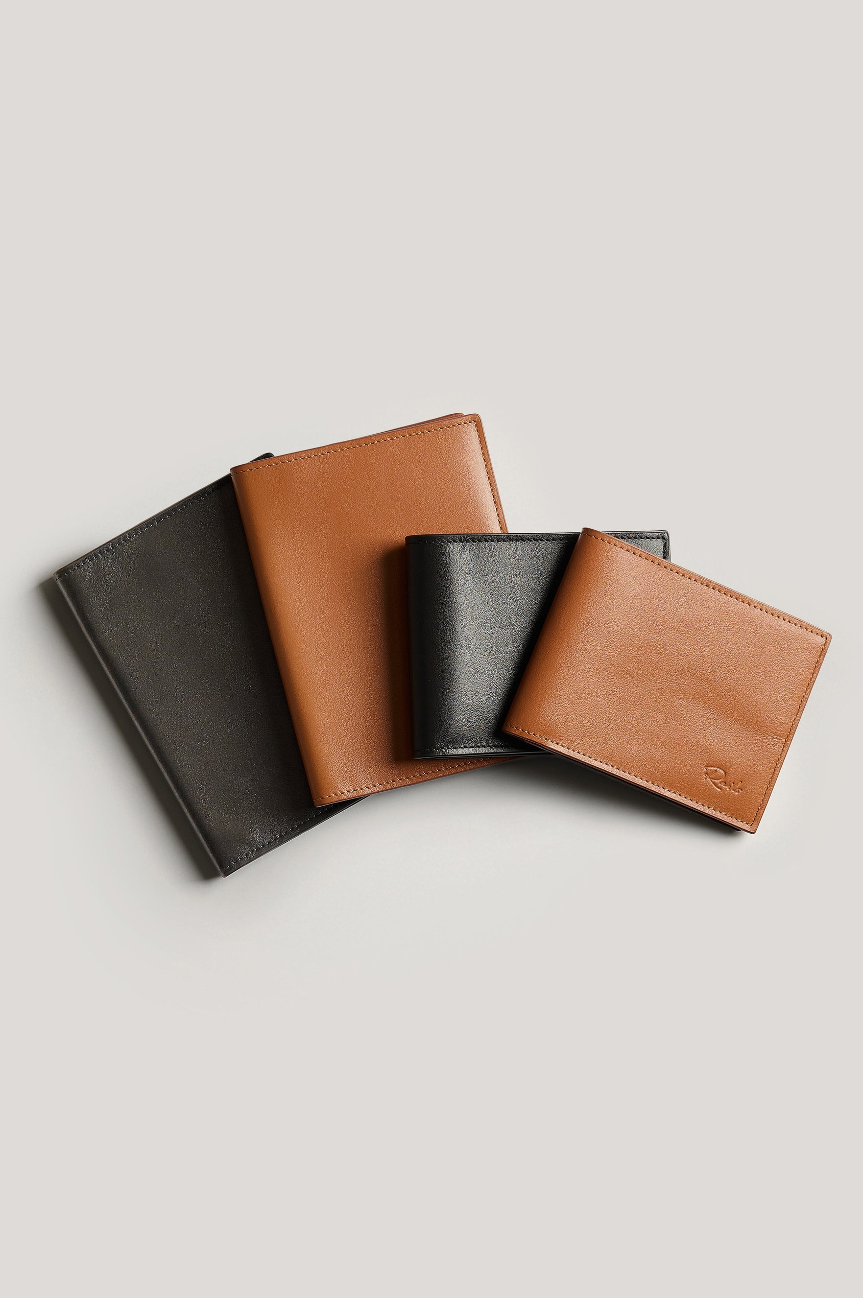Leather passport holder folded, front view next to wallets for size reference, in brown Cognac colorway.