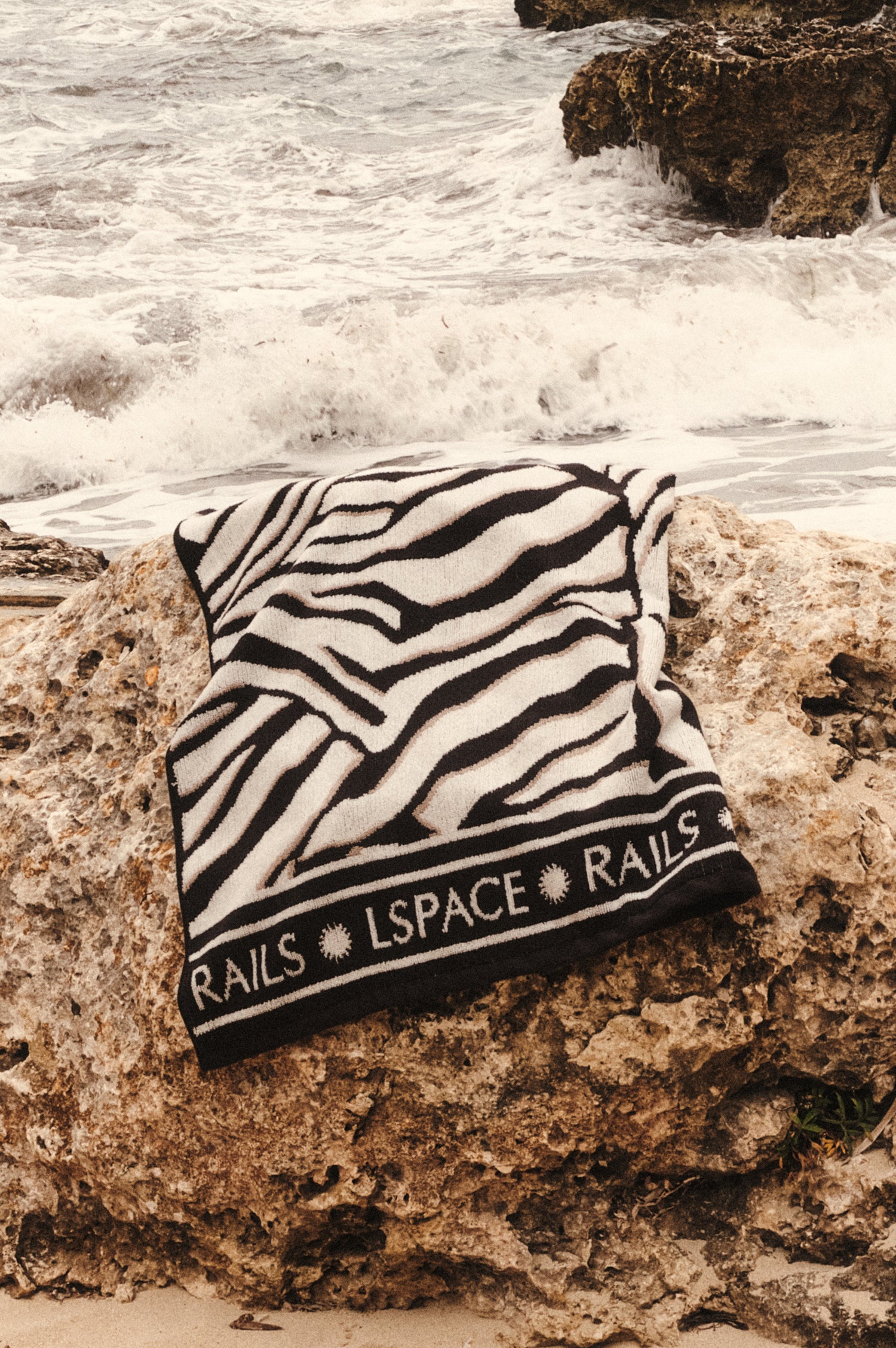 Playa Blanca Towel in Playa Blanca black and white abstract print with Rails and LSpace logo on the edge - stylized view of towel on the beach