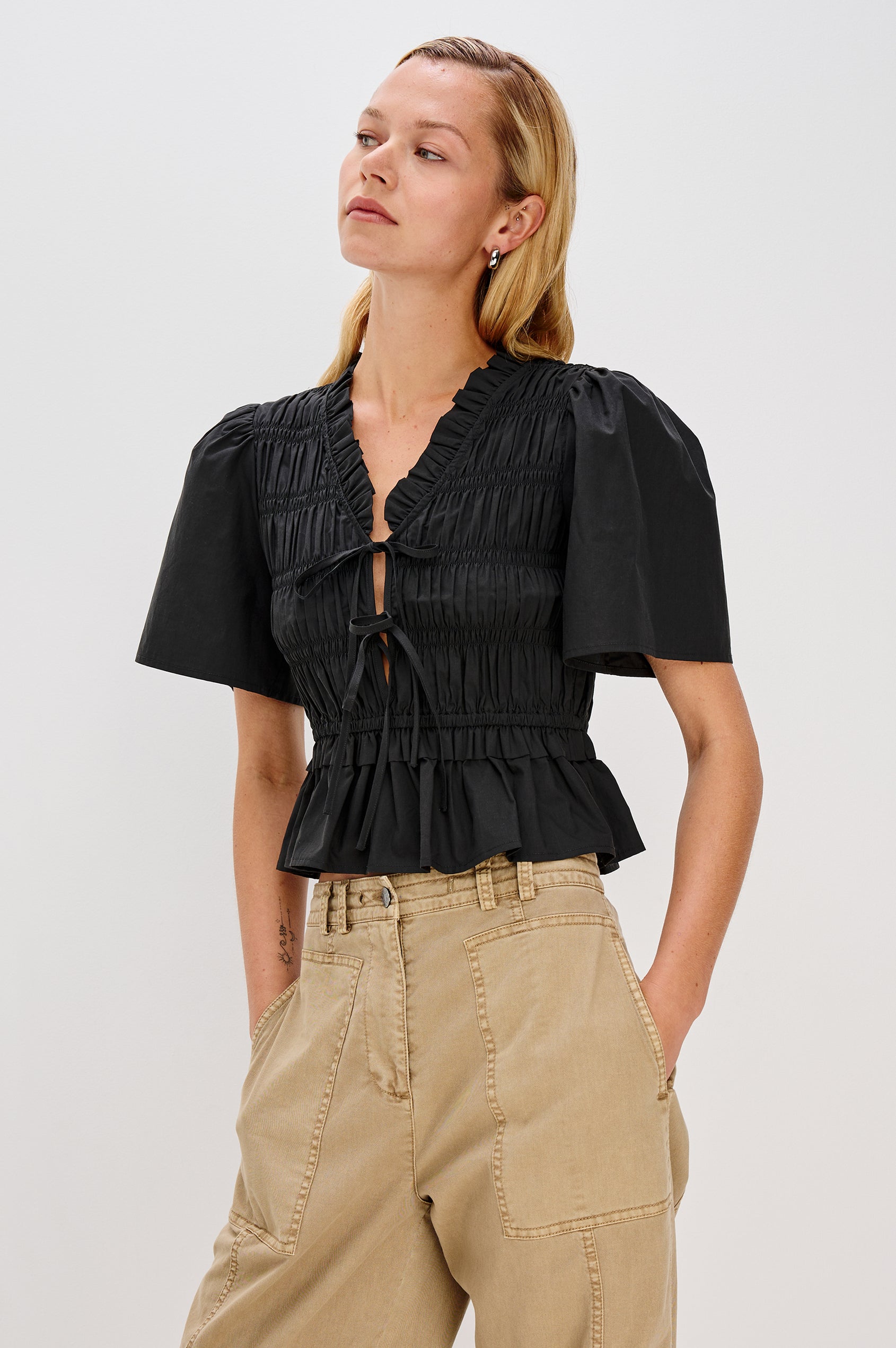 Portia V-Neck Tie Front Top with Short Puff Sleeves and a Ruffled Peplum Hem in Black Colorway. Front View Shown on Model.