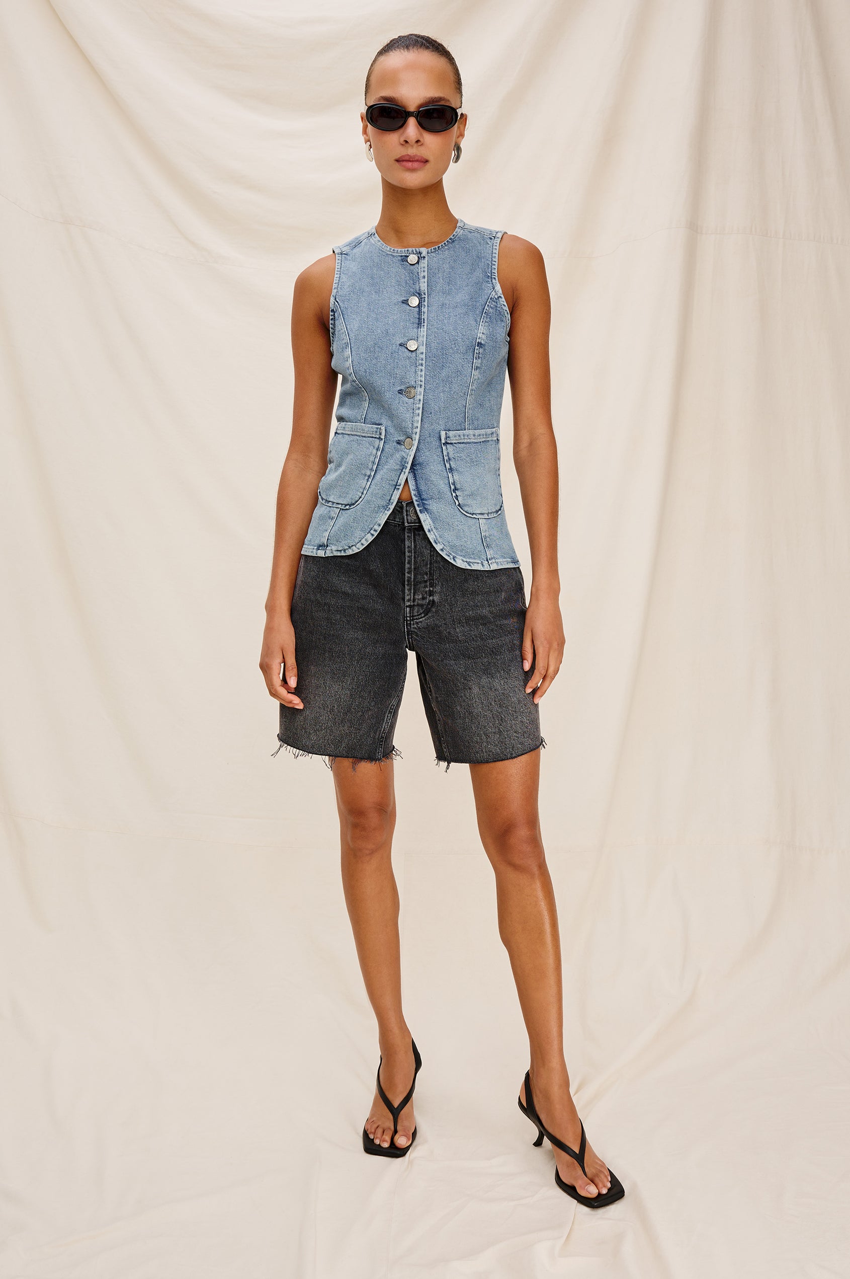 Portola Sleeveless Denim Vest with Exposed Button Front Closure, Crew Neck, Front Patch Pockets and a Scalloped Split Hem in Blue Eyed Girl Colorway. Full Body Front View Shown on Model.