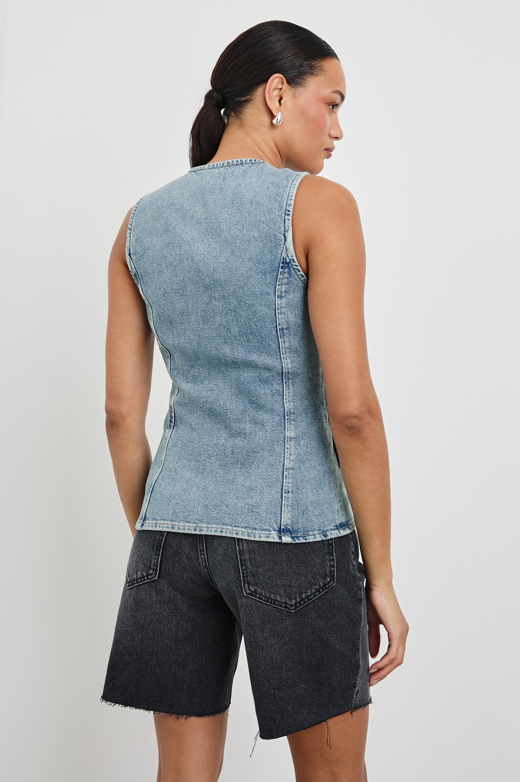 Portola Sleeveless Denim Vest with Exposed Button Front Closure, Crew Neck, Front Patch Pockets and a Scalloped Split Hem in Blue Eyed Girl Colorway. Back View Shown on Model.