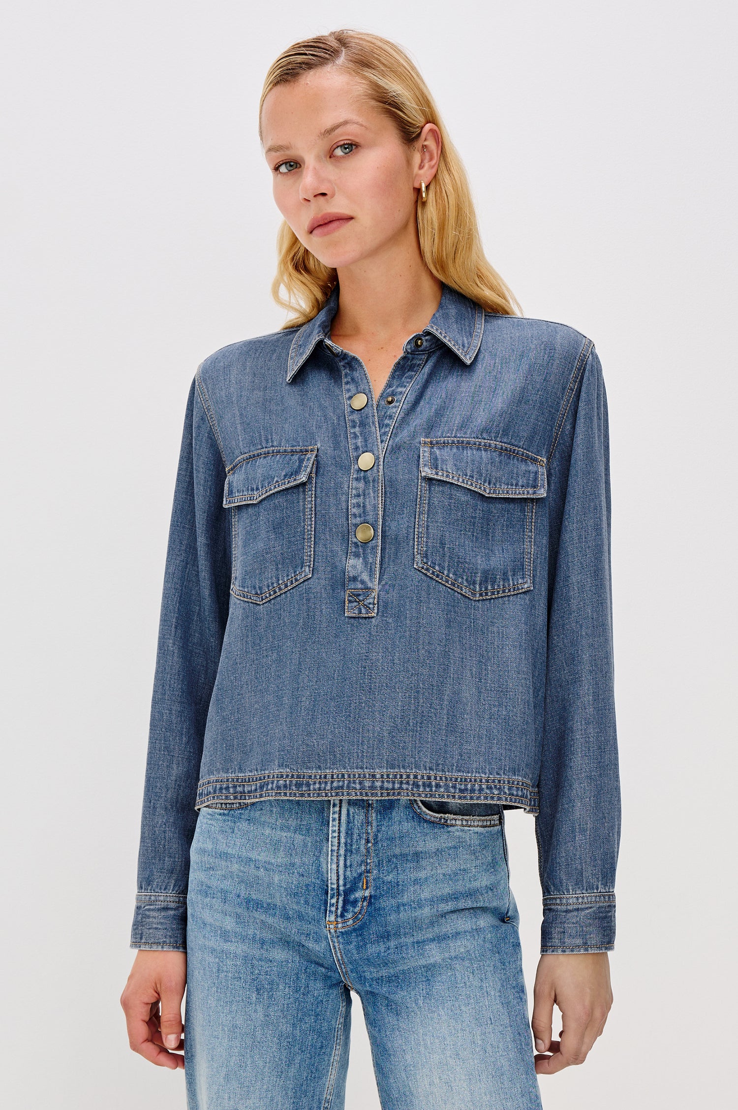 Ports is a soft, lightweight denim shirt with a cropped fit. The shirt features a half placket with snap-front closures, short sleeves, and two chest pockets in Antique Blue Colorway - Front View Featured on Model