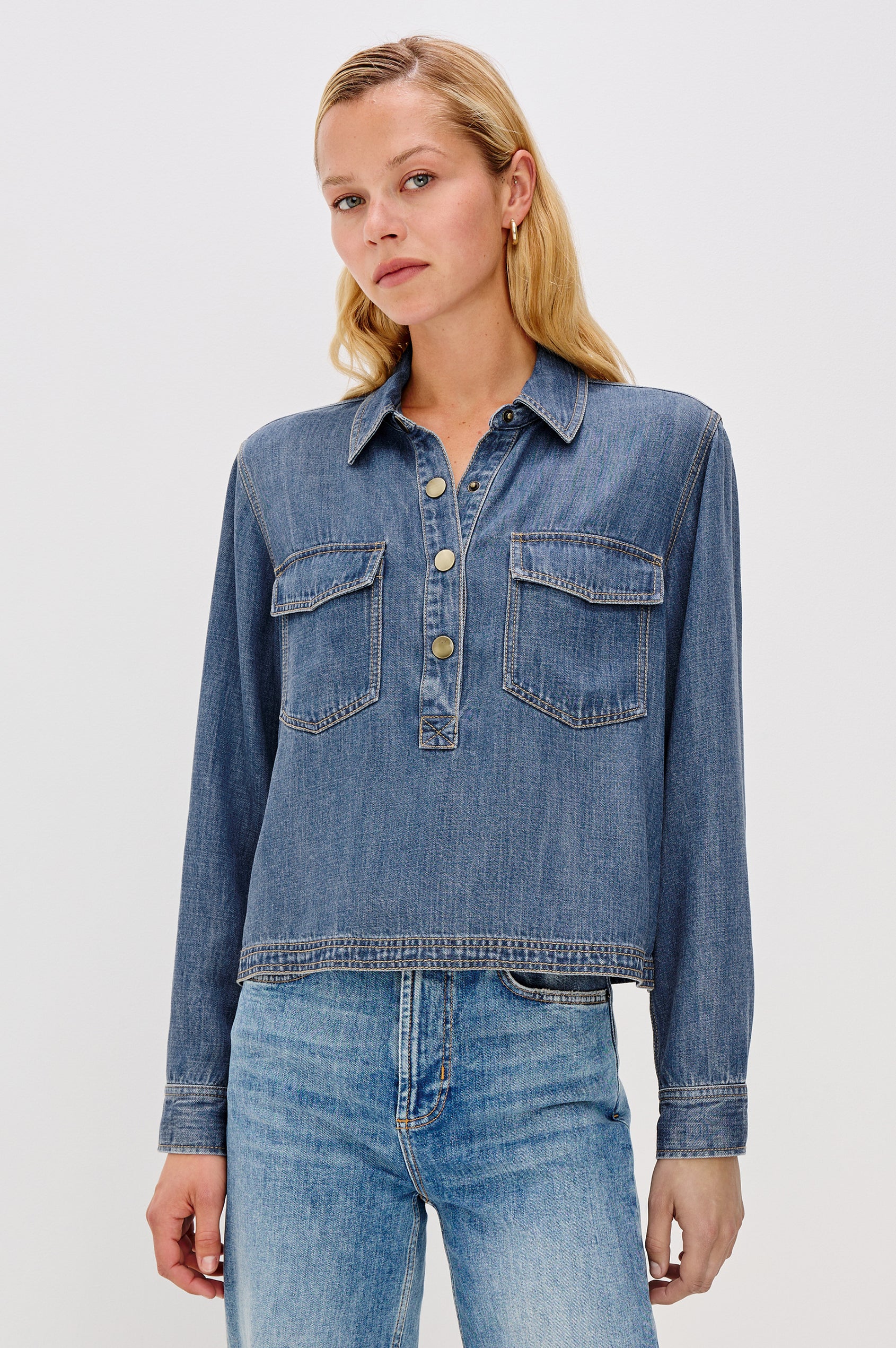 Ports is a soft, lightweight denim shirt with a cropped fit. The shirt features a half placket with snap-front closures, short sleeves, and two chest pockets in Antique Blue Colorway - Front View Featured on Model
