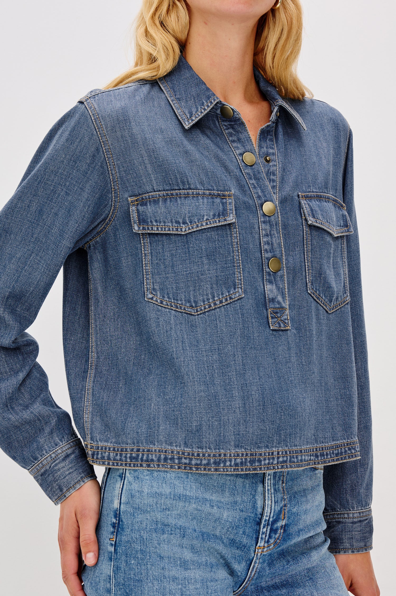 Ports is a soft, lightweight denim shirt with a cropped fit. The shirt features a half placket with snap-front closures, short sleeves, and two chest pockets in Antique Blue Colorway - Close up of Details on model