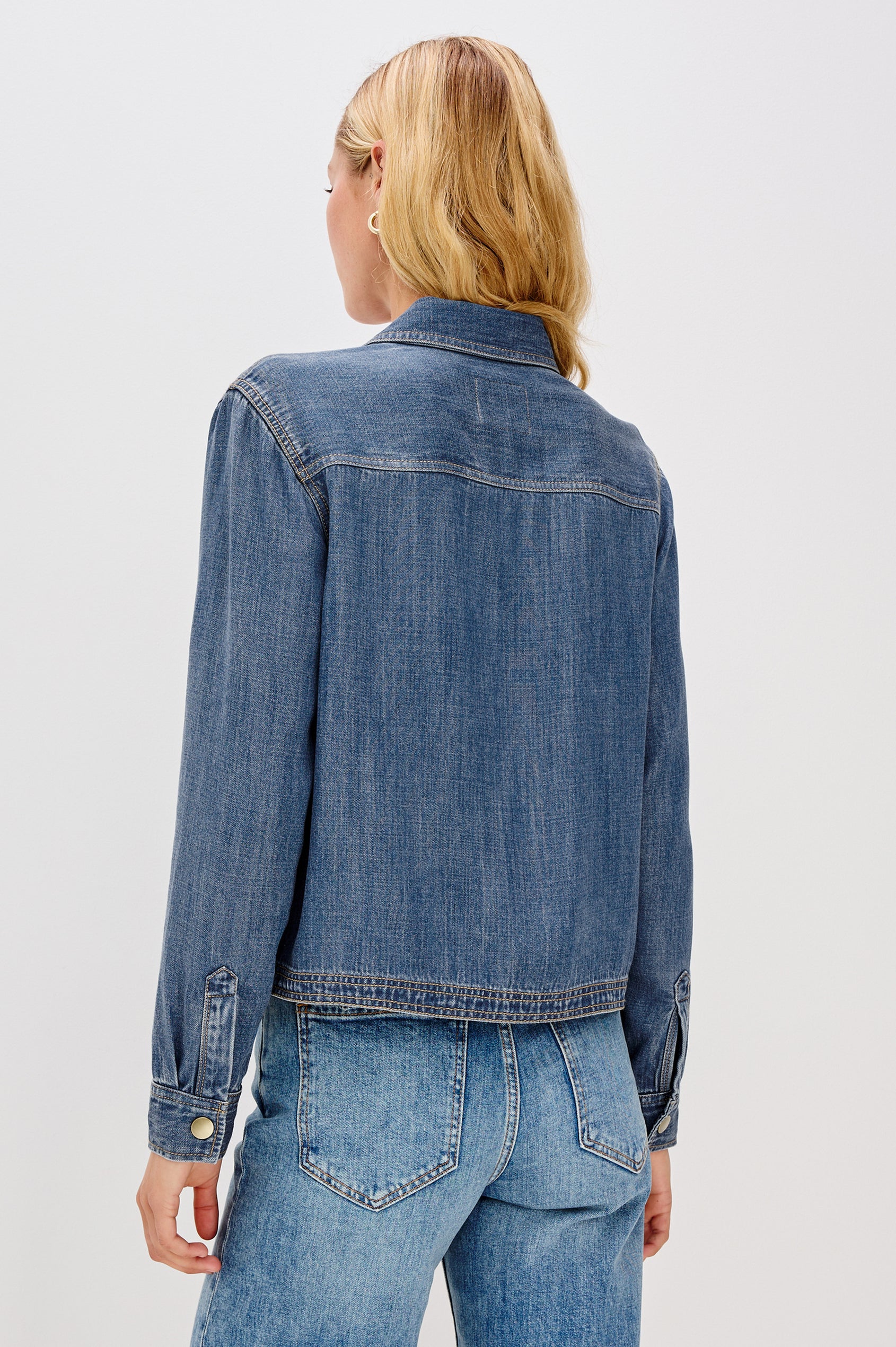Ports is a soft, lightweight denim shirt with a cropped fit. The shirt features a half placket with snap-front closures, short sleeves, and two chest pockets in Antique Blue Colorway - Back View Featured on Model