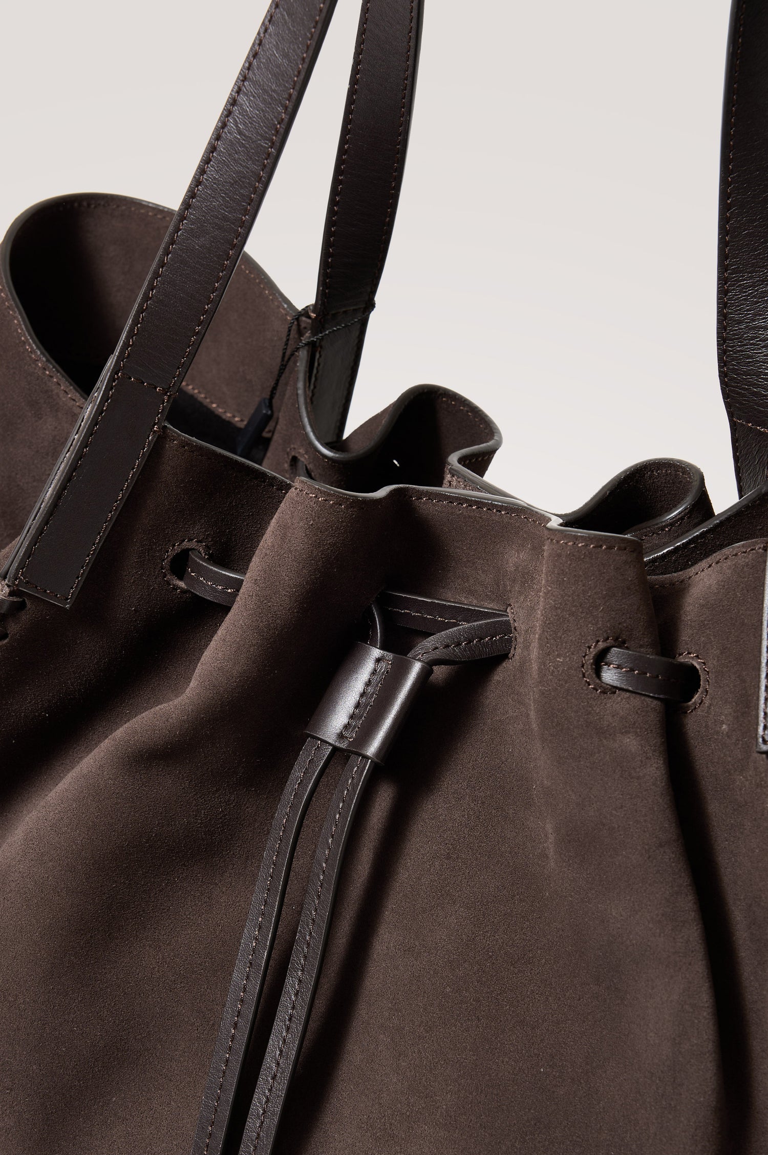 Prato Bucket Tote in Suede With Whipstitch Trim, Fixed Top Straps, Drawcord Closure, Interior Zip Pocket, Interior Slip Pocket in Dark Brown Suede Colorway - Front Close Up Product View Featured