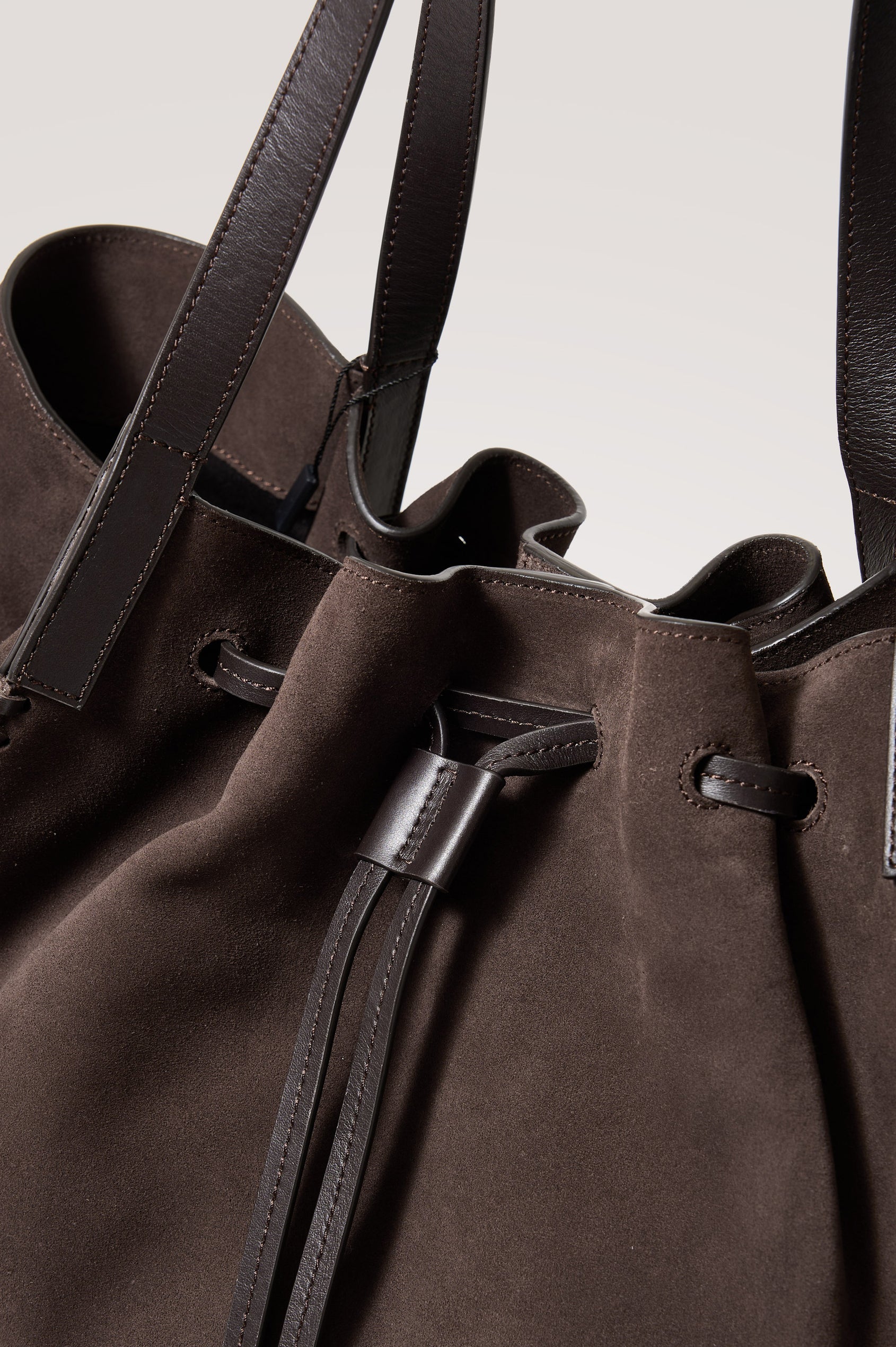 Prato Bucket Tote in Suede With Whipstitch Trim, Fixed Top Straps, Drawcord Closure, Interior Zip Pocket, Interior Slip Pocket in Dark Brown Suede Colorway - Front Close Up Product View Featured
