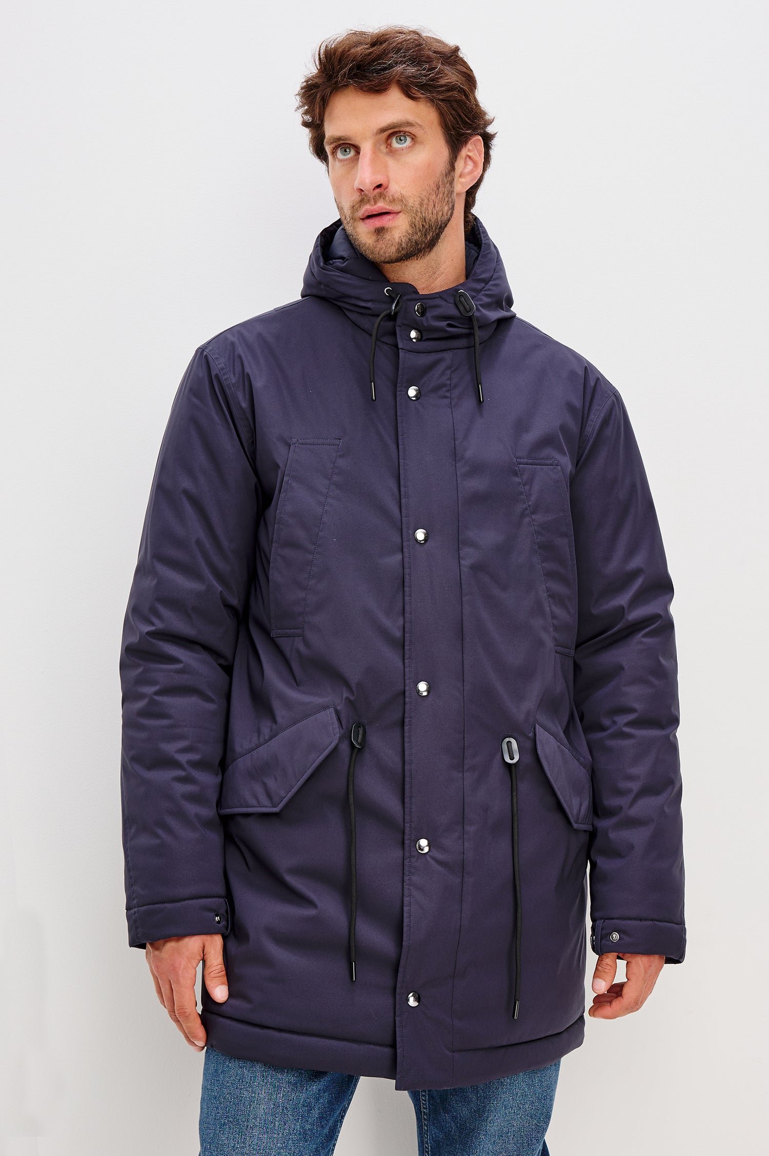 Rainier is a hooded parka coat, water-resistant and features hand warming pockets with snap closure, drawcord at hood and waist for sinching effect and a double flap center front closure and back seam vent in Navy colorway. Front view featured on model.