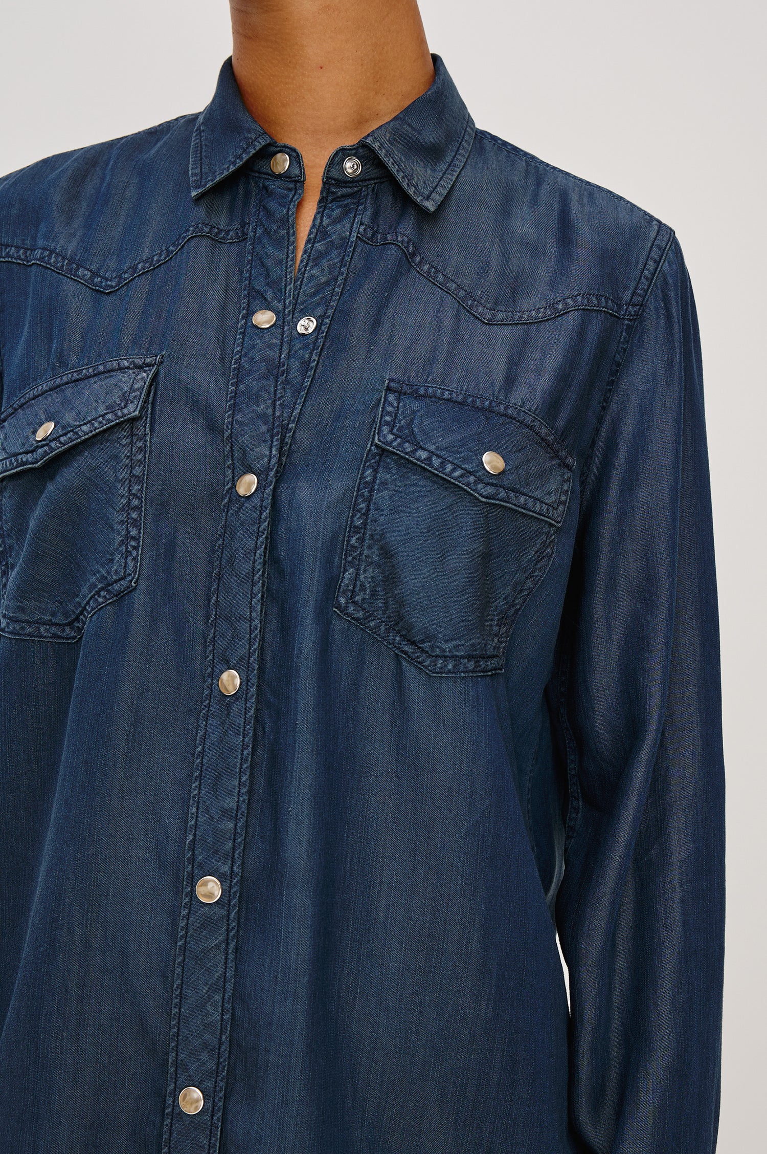 Remi is a utility-style Tencel denim shirt with a relaxed fit. The shirt features a notched collar, two front flap pockets, and faux horn buttons etched with a logo in Oceana dark blue colorway - Close up of Details on Model