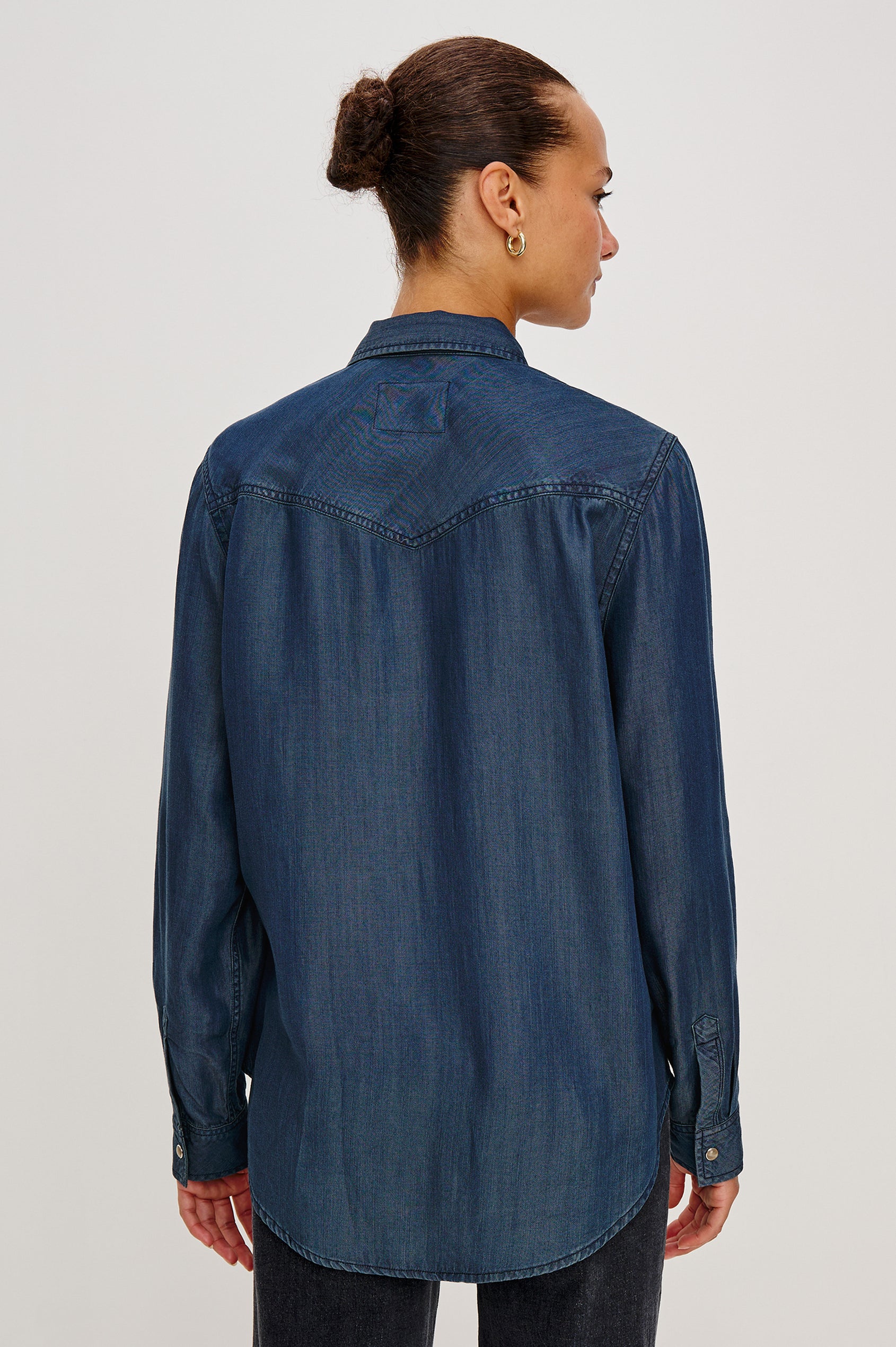 Remi is a utility-style Tencel denim shirt with a relaxed fit. The shirt features a notched collar, two front flap pockets, and faux horn buttons etched with a logo in Oceana dark blue colorway - Back View Featured on Model