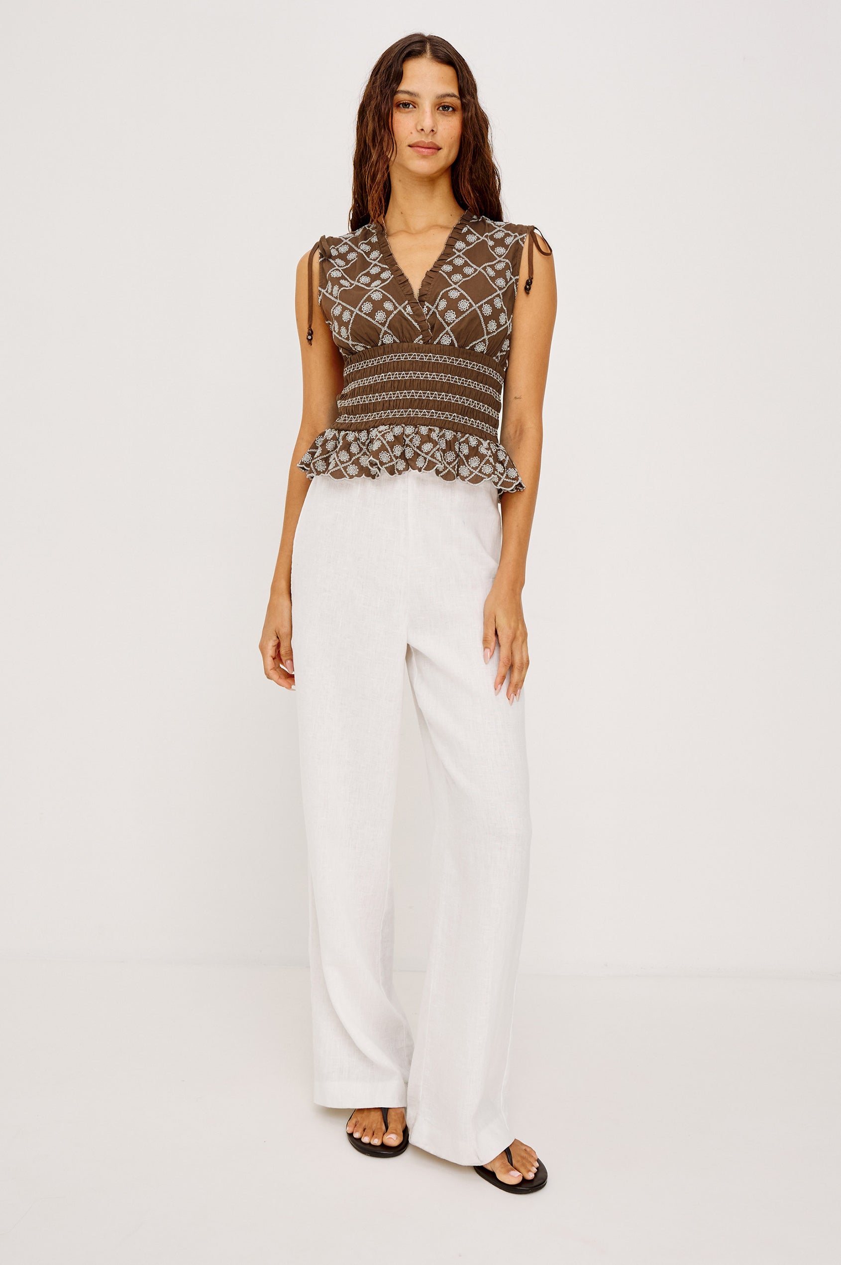 Rizzo Sleeveless Top in Cotton Voile With V-Neckline, Shoulder Ties, Ruffle Trim, Smocked Waist, and Peplum Hem in Cocoa Daisy Embroidery Colorway - Full Body Front View Featued on Model