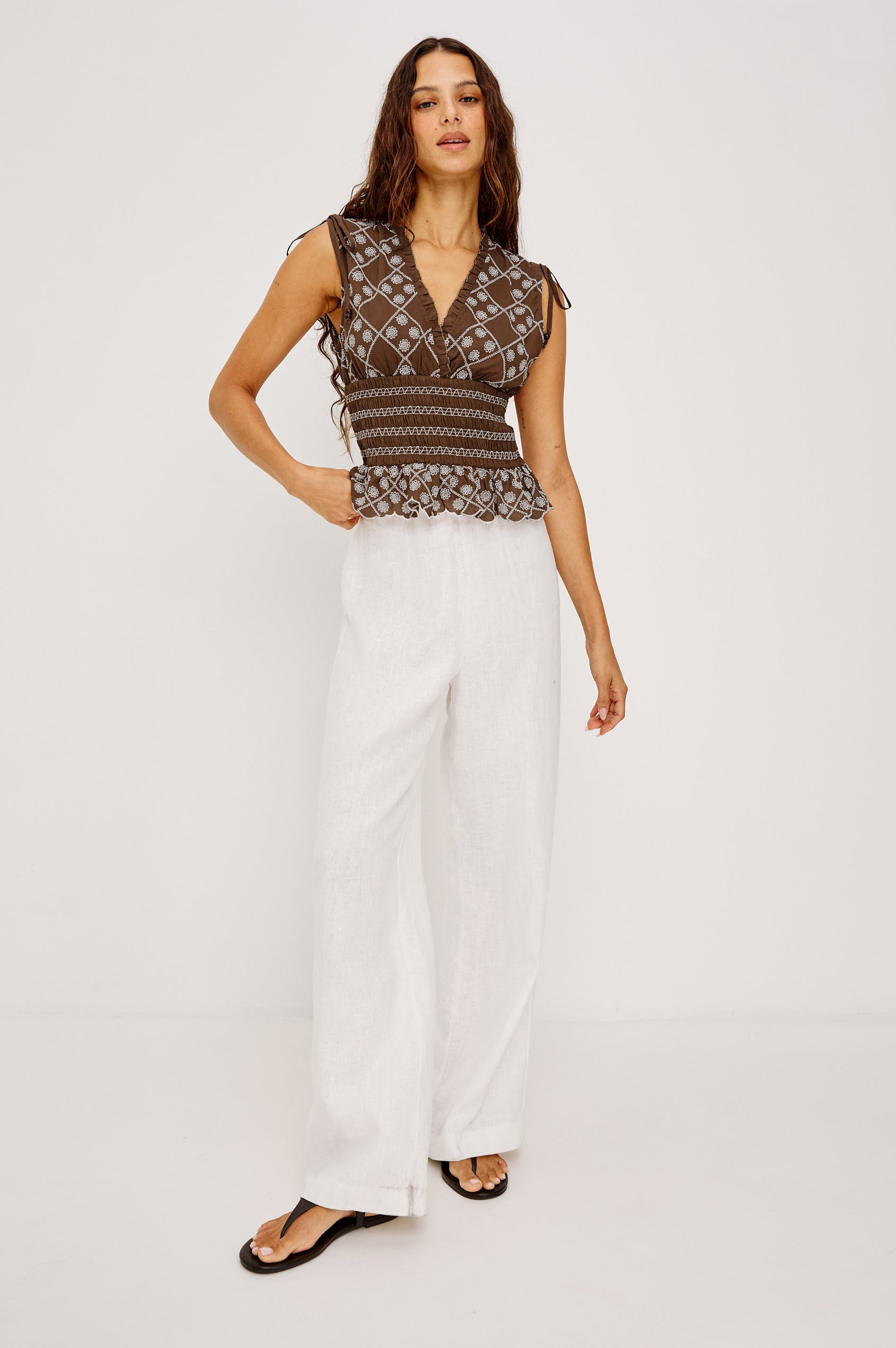 Rizzo Sleeveless Top in Cotton Voile With V-Neckline, Shoulder Ties, Ruffle Trim, Smocked Waist, and Peplum Hem in Cocoa Daisy Embroidery Colorway - Full Body Front View Featued on Model