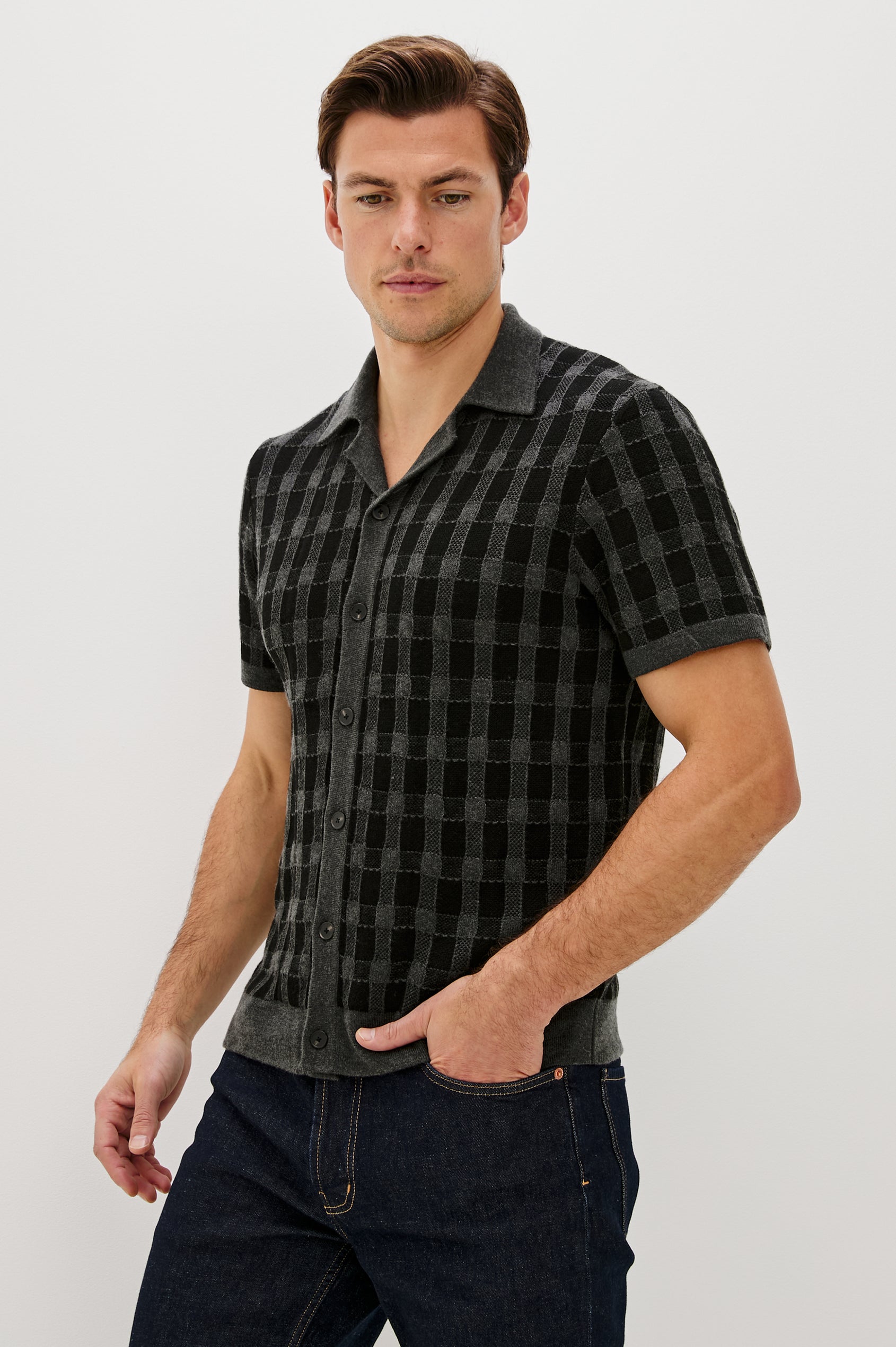 The Ronan is a collared button front knit shirt with short sleeves, grey rib trim, grey + black block stitch pattern in Charcoal Black colorway. Front view featured on model.