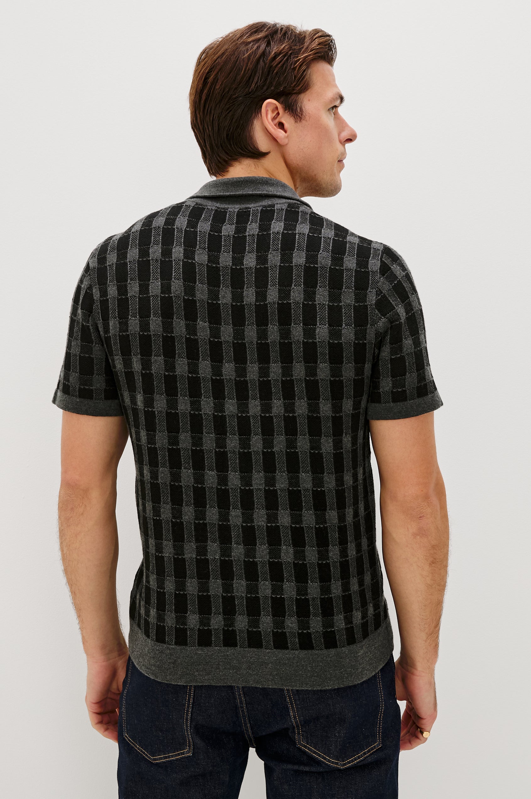 The Ronan is a collared button front knit shirt with short sleeves, grey rib trim, grey + black block stitch pattern in Charcoal Black colorway. Back view featured on model.