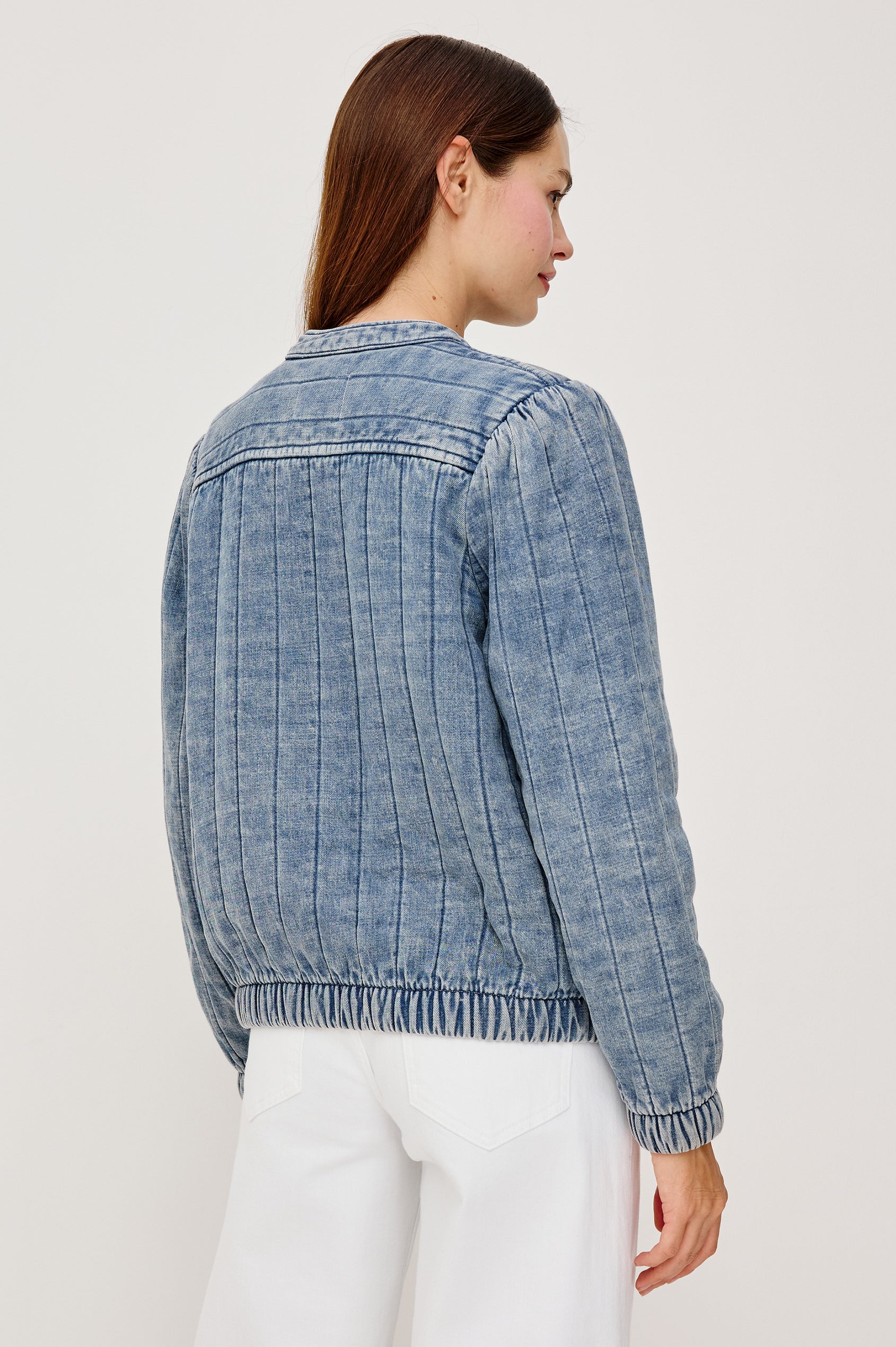 The Rosell is a boxy bomber jacket in ultra-soft quilted washed denim with snap button closures, elastic cuffs and hem, and long puff sleeves. Back view featured on model.