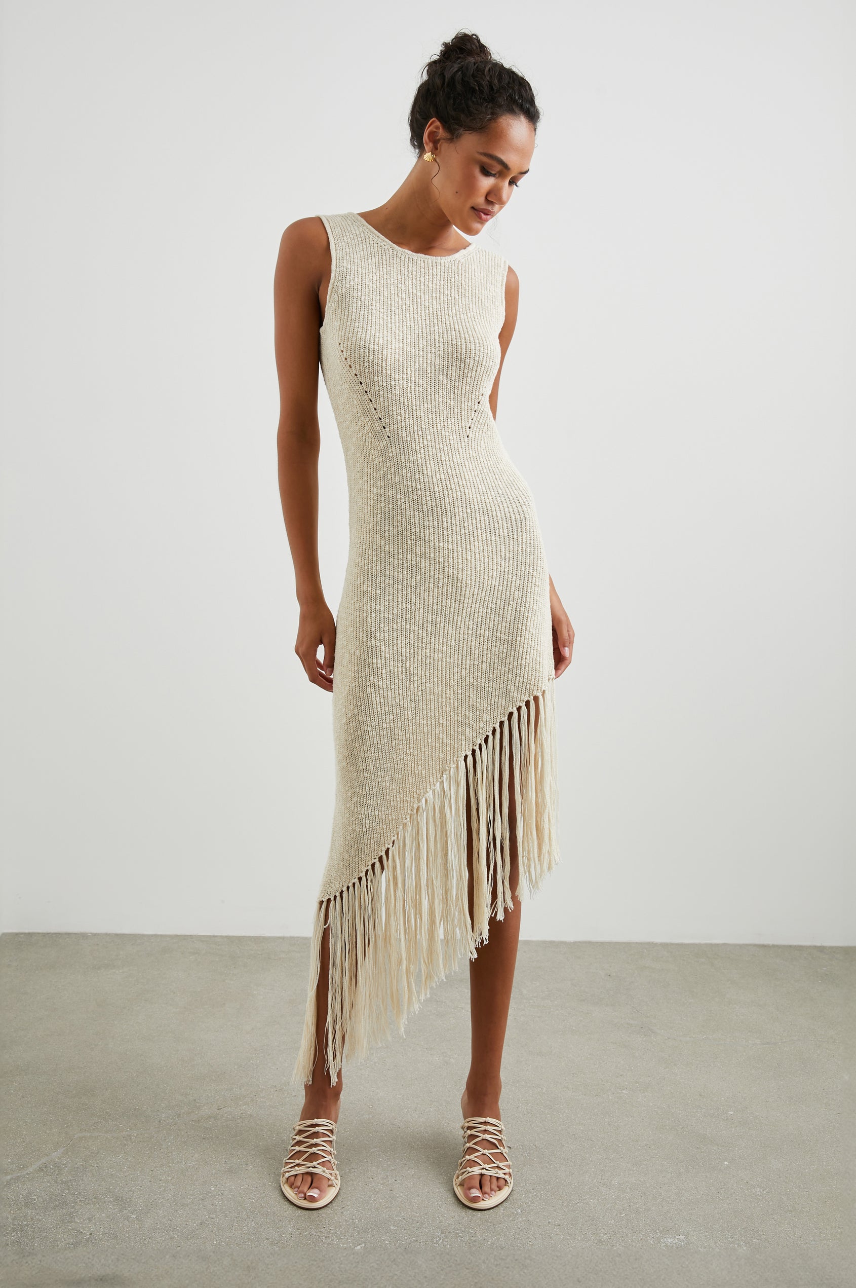 Rylee Sleeveless Ribbed Dress with a Scoop Neck, and a Fringed Asymmetrical Hemline from the Upper Thigh to the Knee in Ecru Colorway - Front Full Body View Featured on Model