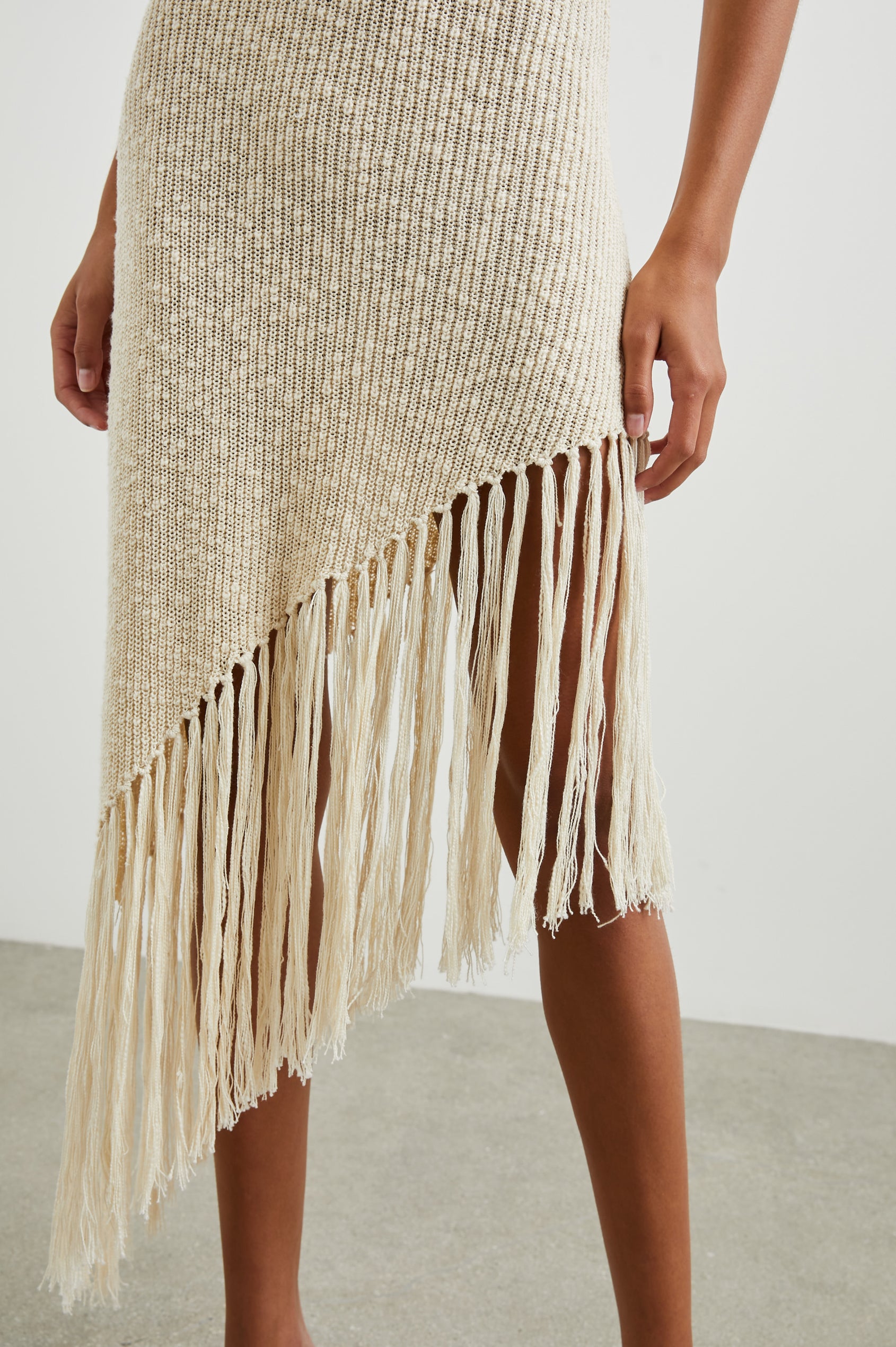Rylee Sleeveless Ribbed Dress with a Scoop Neck, and a Fringed Asymmetrical Hemline from the Upper Thigh to the Knee in Ecru Colorway - Front View Featured on Model
