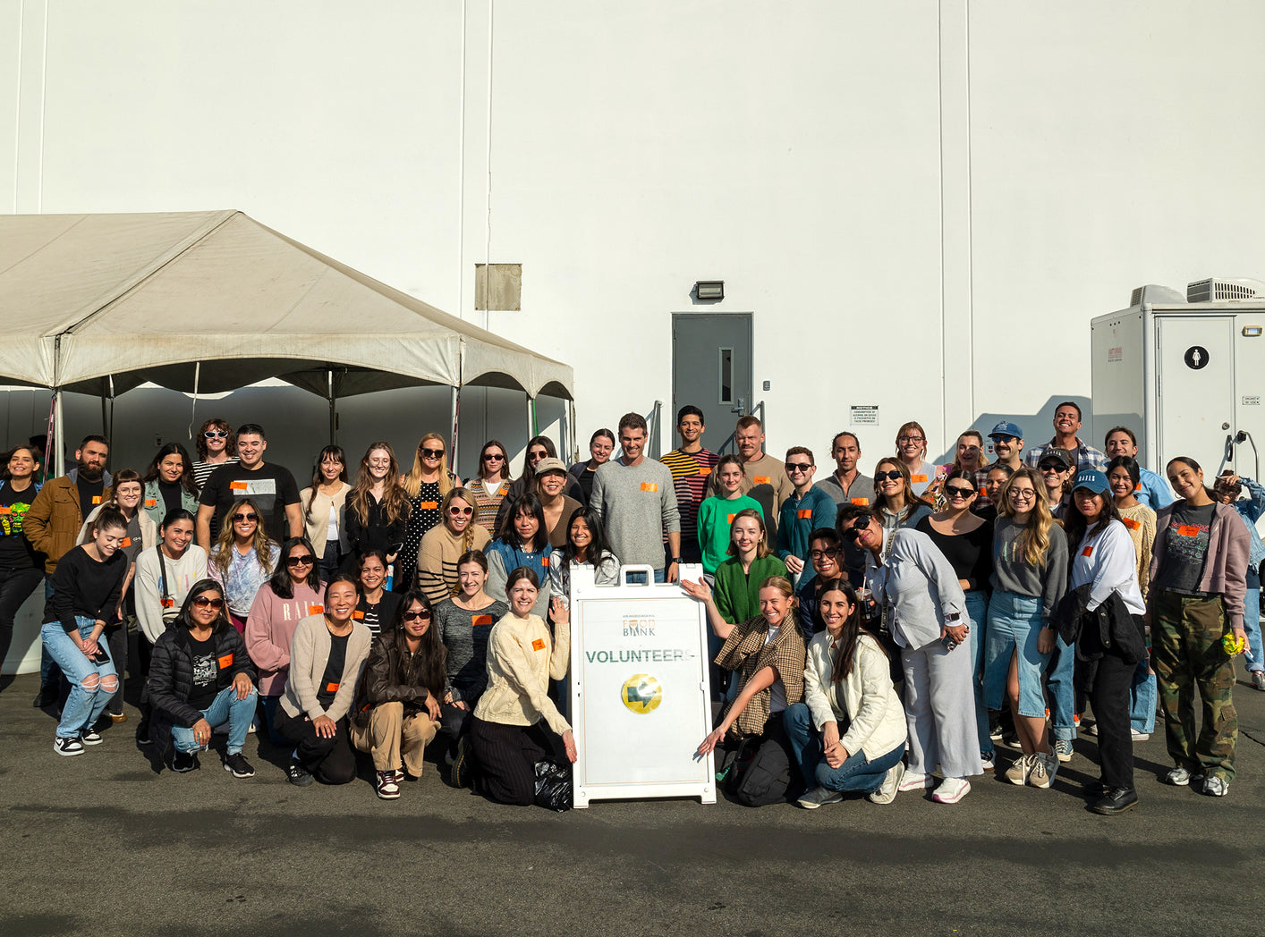 LARGE GROUP OF EMPLOYEES GATHERED AROUND A VOLUNTEER EVENT SIGN